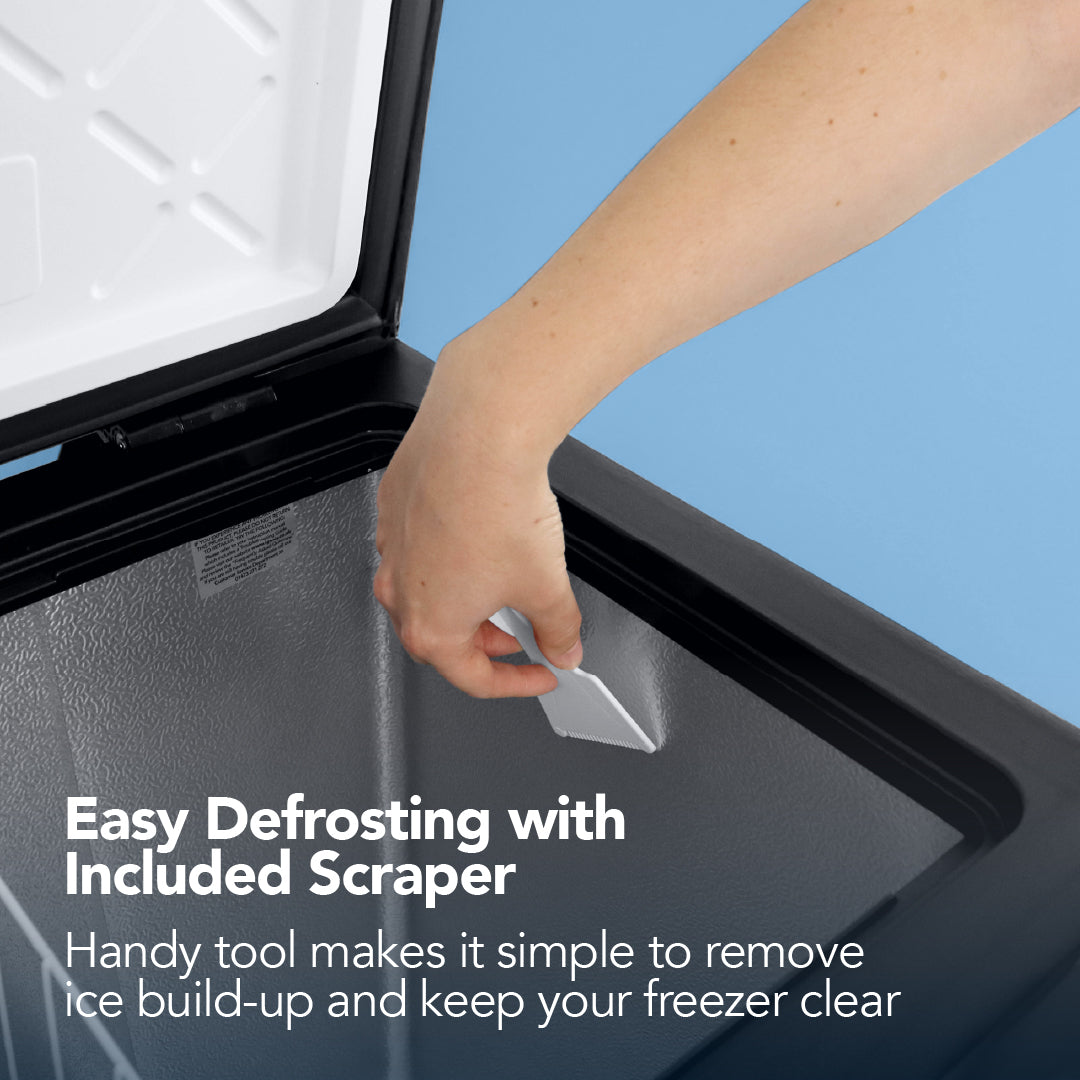 A hand uses the included scraper to remove ice from an open Igenix Freestanding Chest Freezer, 99 Litre, Black. Text reads: Easy Defrosting with Included Scraper—keep your extra freezer storage clear and ice-free.