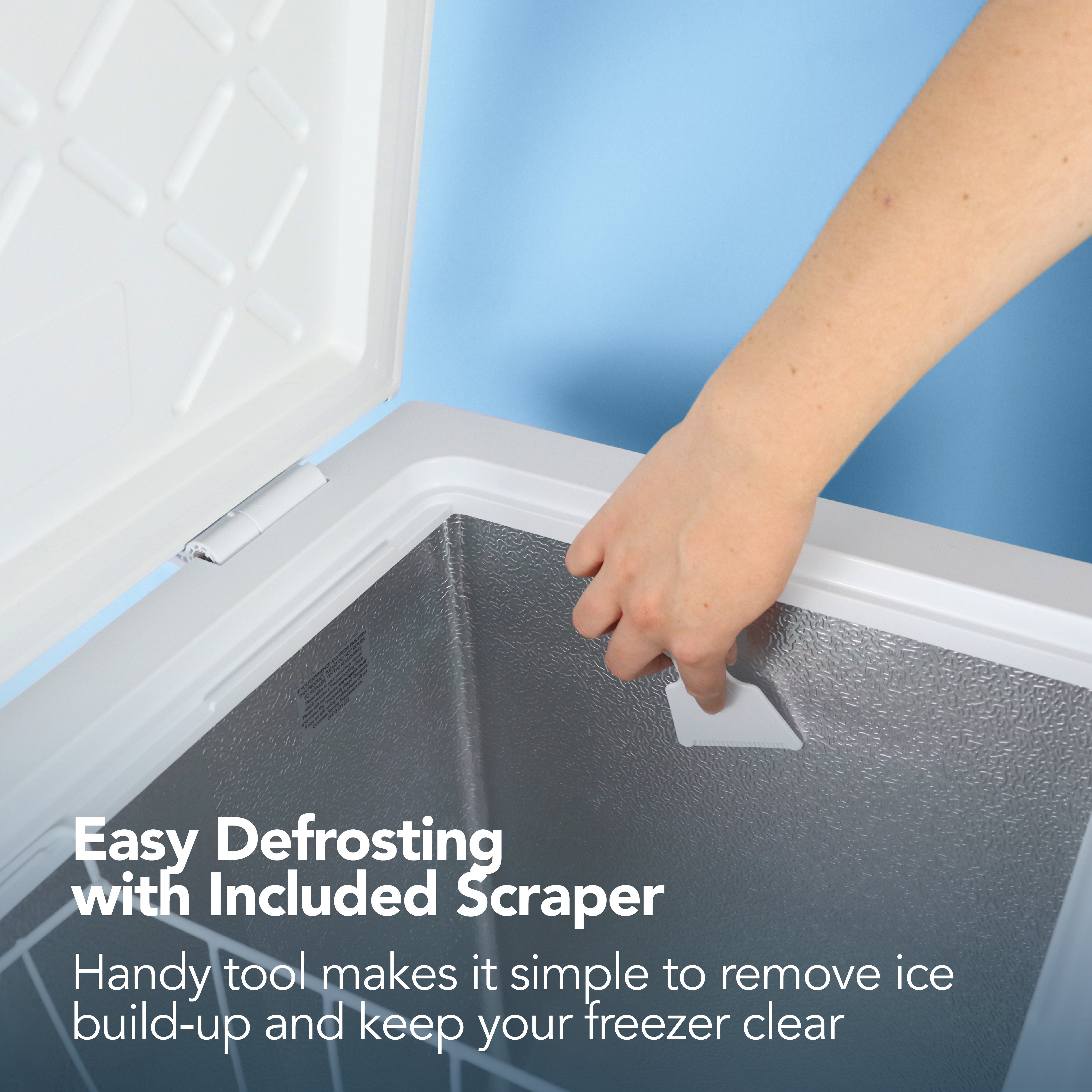 A hand uses the included white plastic scraper to remove ice from the Igenix Freestanding Chest Freezer, 99 Litre, White—ideal as a secondary freezer. Easily defrost and keep extra storage space clear with this practical appliance.