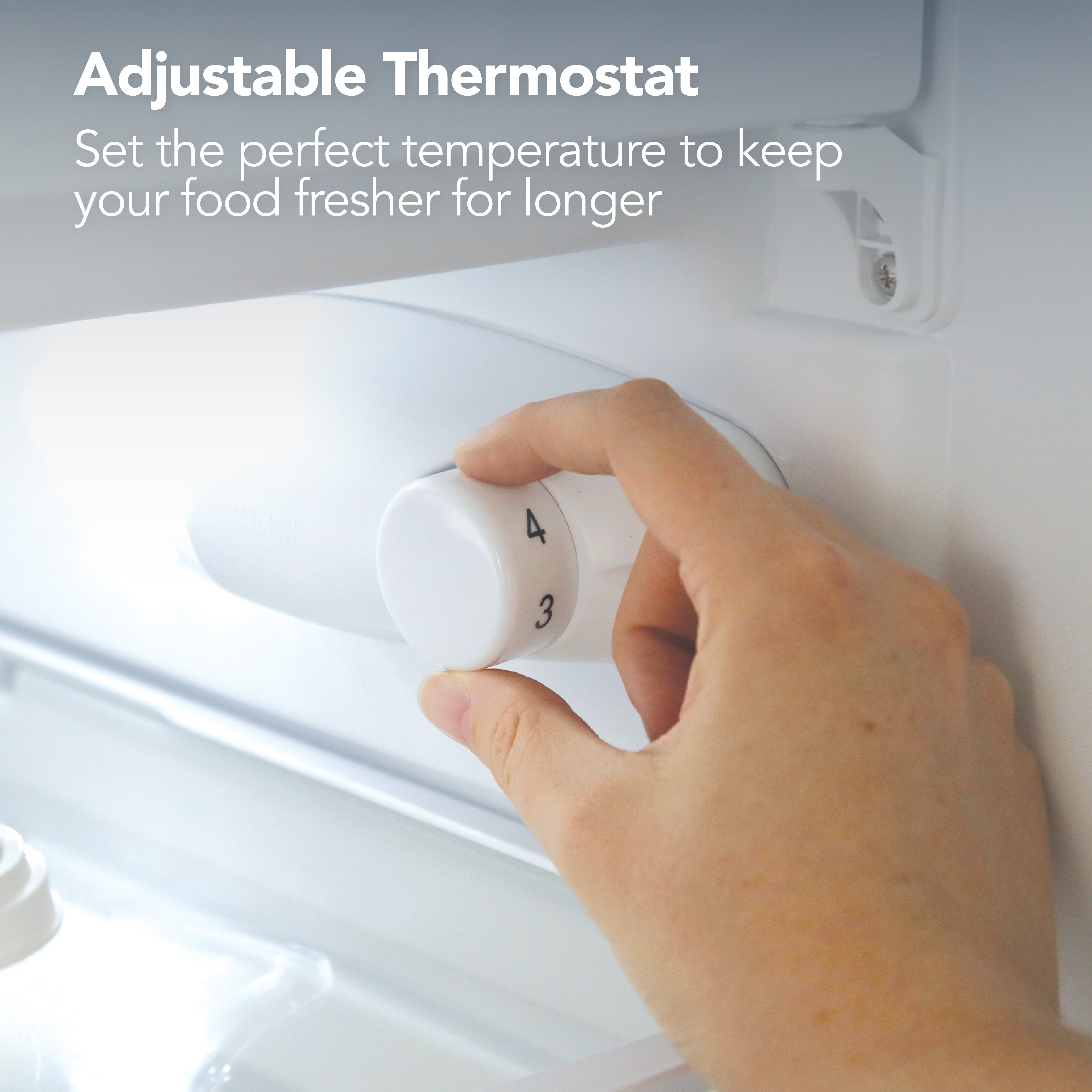 A hand turns the temperature dial inside the Igenix Under Counter Fridge with Ice Box, White. Text above: Adjustable Thermostat. Easily set the ideal temperature to keep your food fresher for longer.