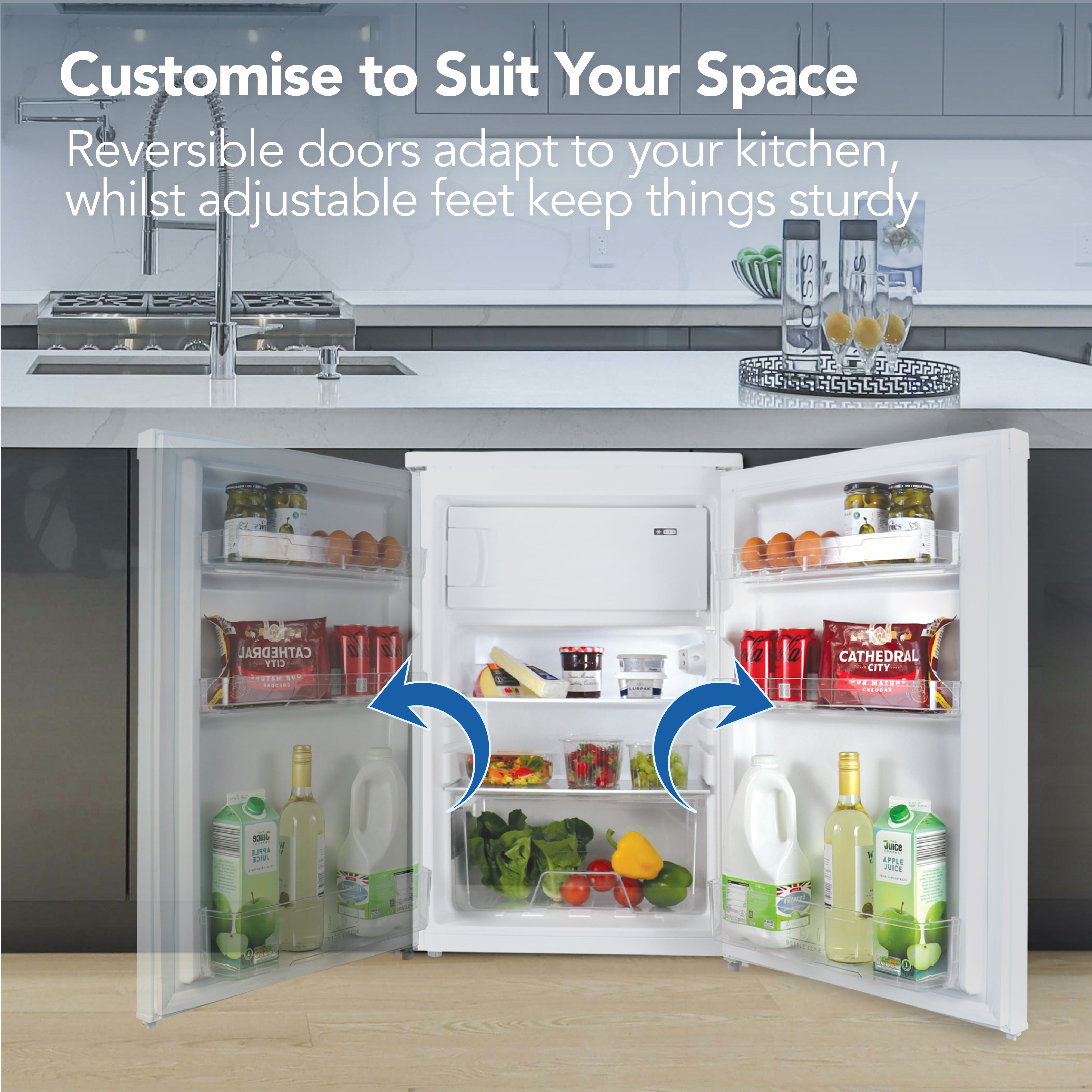 The Igenix Under Counter Fridge with Ice Box, shown with both reversible doors open, reveals stocked shelves for drinks, cheese, milk, and vegetables. The compact white unit fits under the kitchen counter and features an adjustable thermostat.