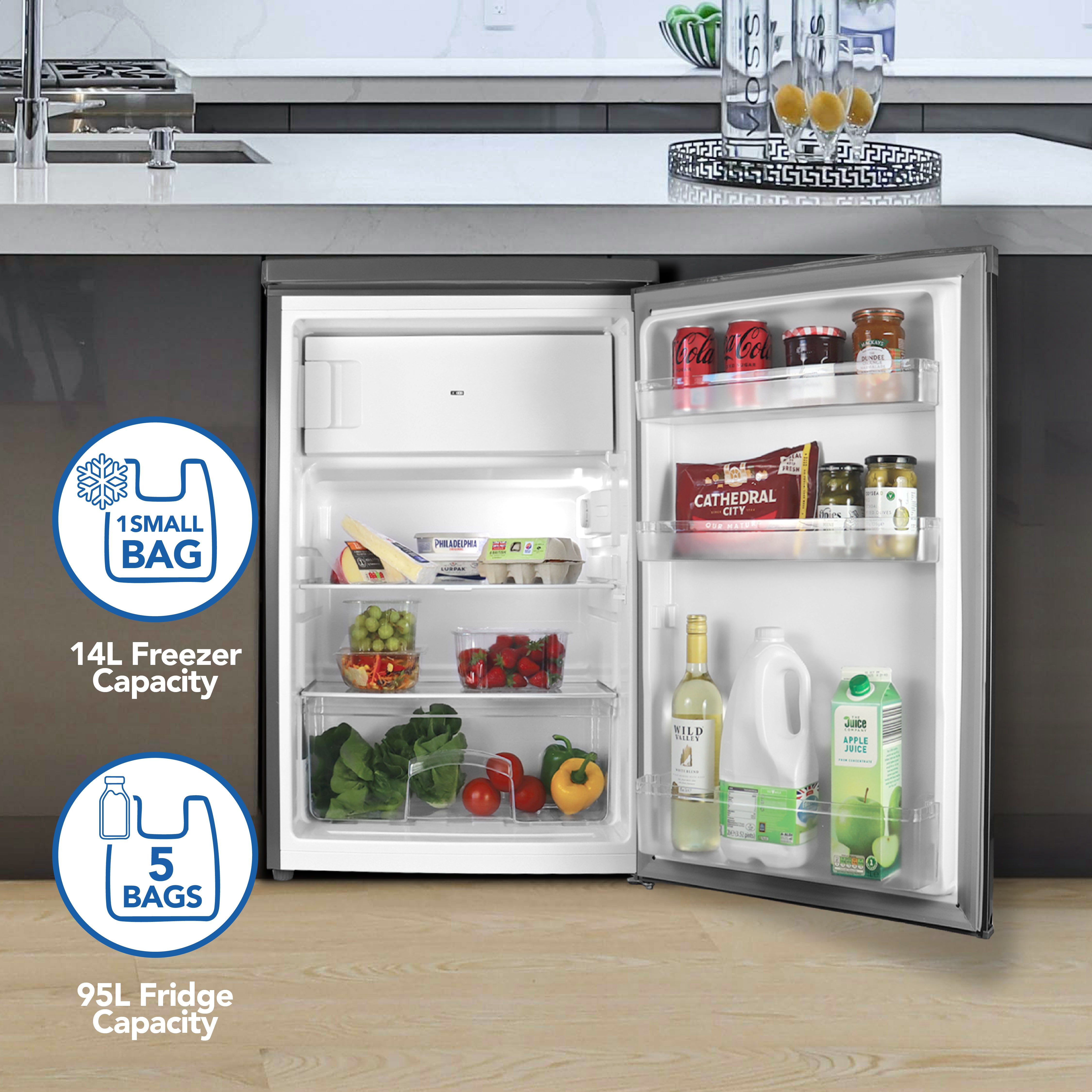 The Igenix Under Counter Fridge with Ice Box (Inox) features a 95L fridge (fits 5 bags) and a 14L freezer (fits 1 small bag). Inside, milk, juice, cheese, fruit, and jars are visible in its compact design.