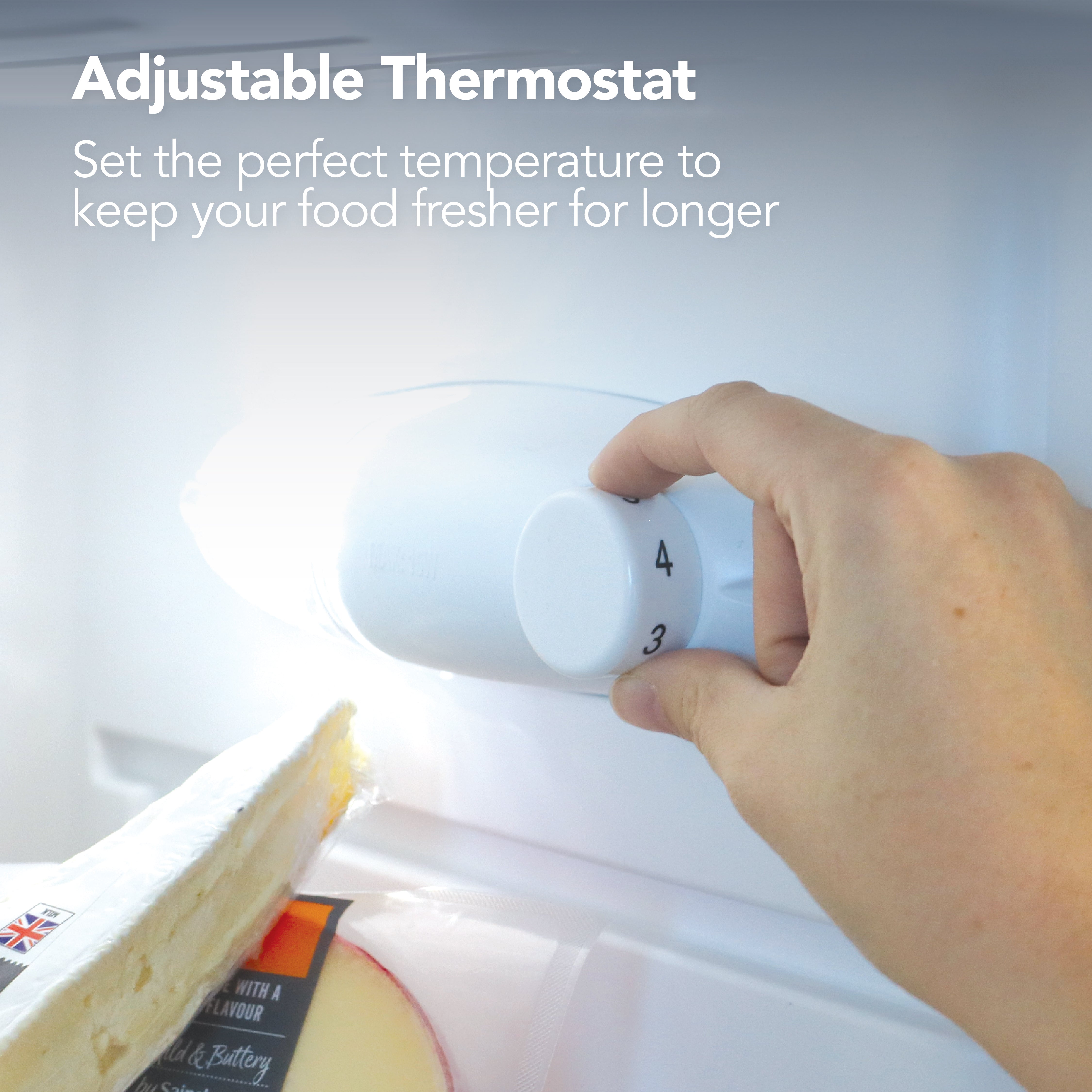 A hand adjusts the temperature dial in the Igenix Under Counter Larder Fridge, 131 Litre, White. Text above: Adjustable Thermostat – Set the ideal temperature to keep your food fresher for longer. Cheese and a salad drawer are visible inside.