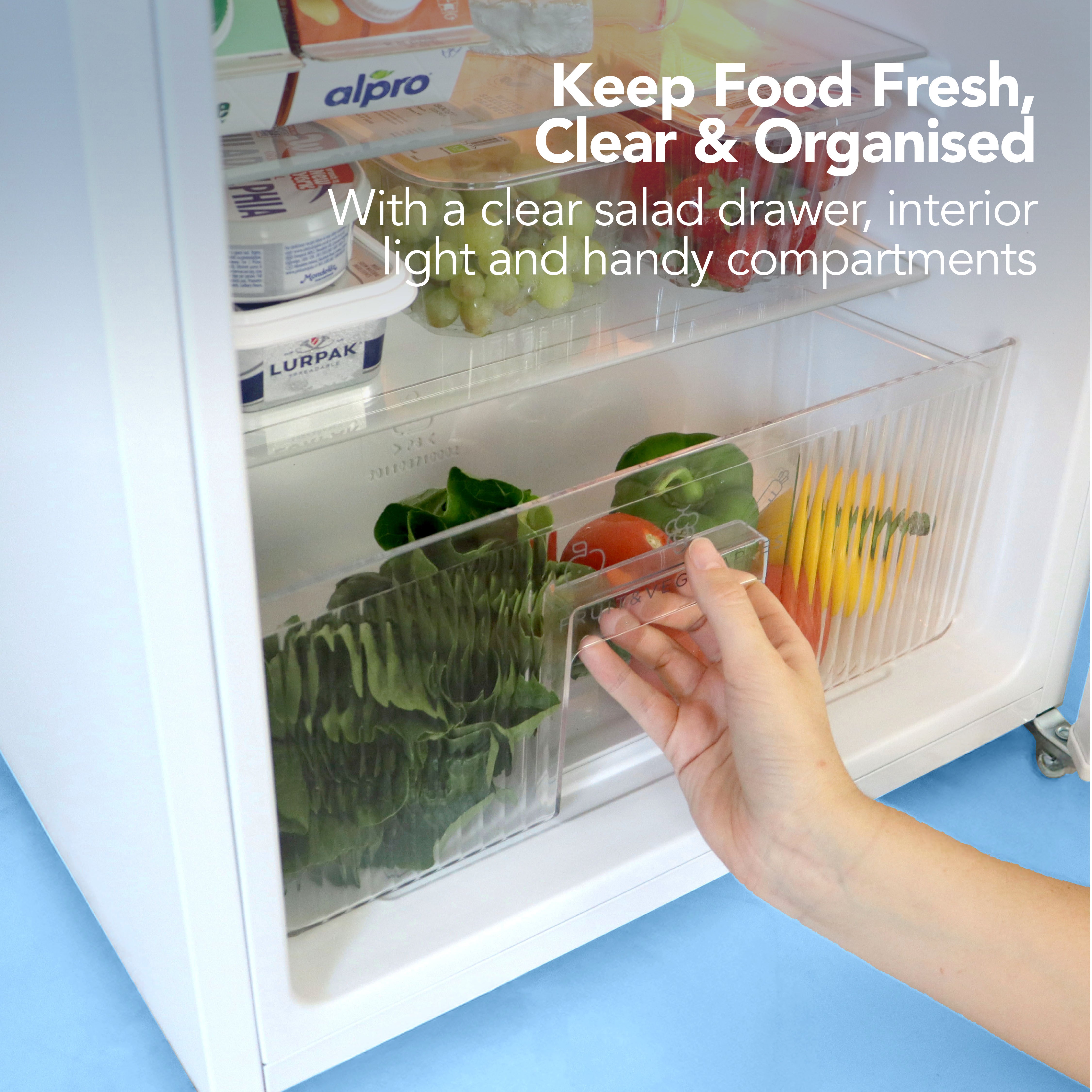 A hand opens an Igenix Under Counter Fridge Freezer (87 L, White), revealing fresh veggies in clear, organised compartments. This energy-efficient fridge features an interior light. Text: Keep Food Fresh, Clear & Organised.