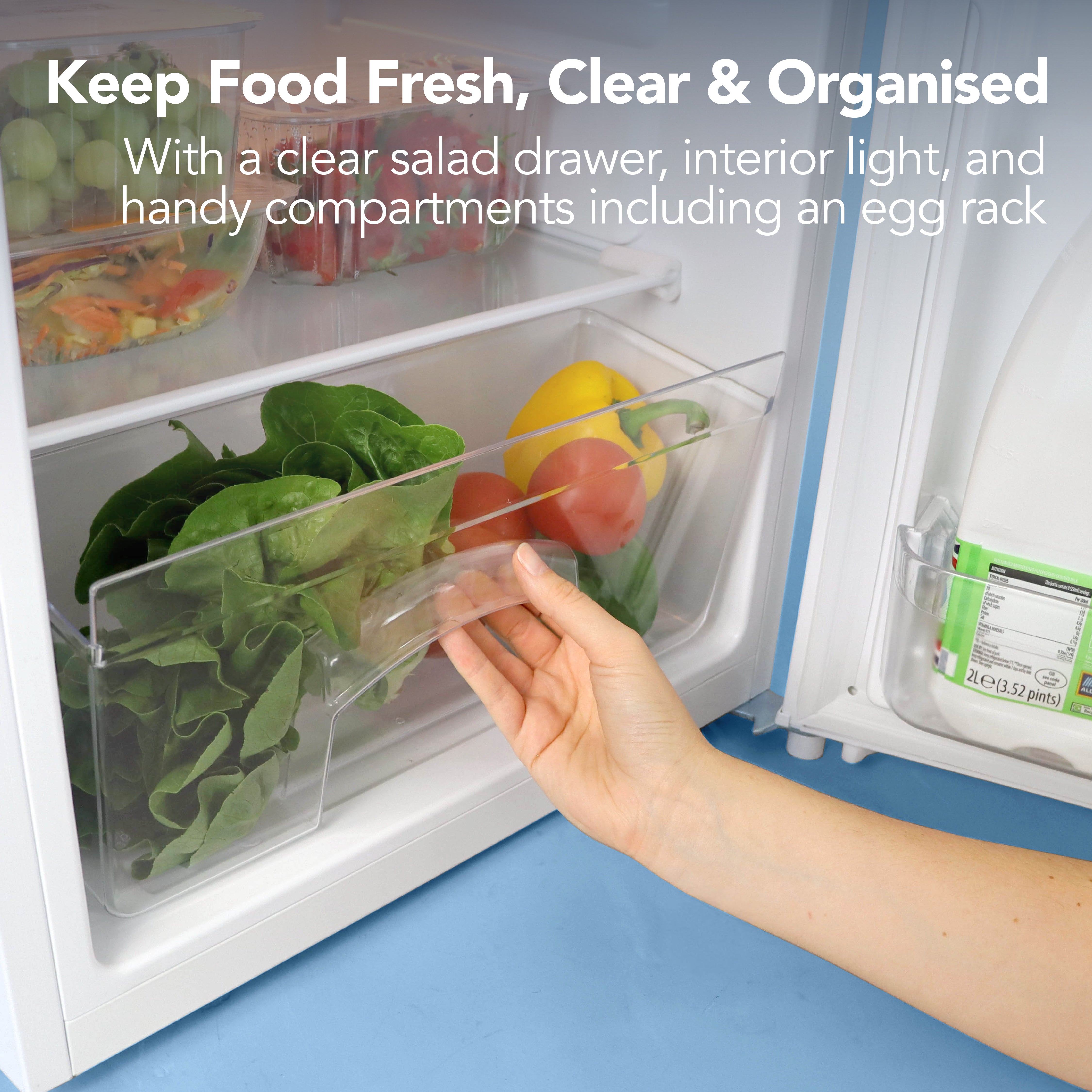 A hand opens a clear salad drawer inside the Igenix Under Counter Fridge with Ice Box (81L, White), revealing fresh veggies. Text: “Keep Food Fresh, Clear & Organised” plus details on reversible doors and handy fridge features.
