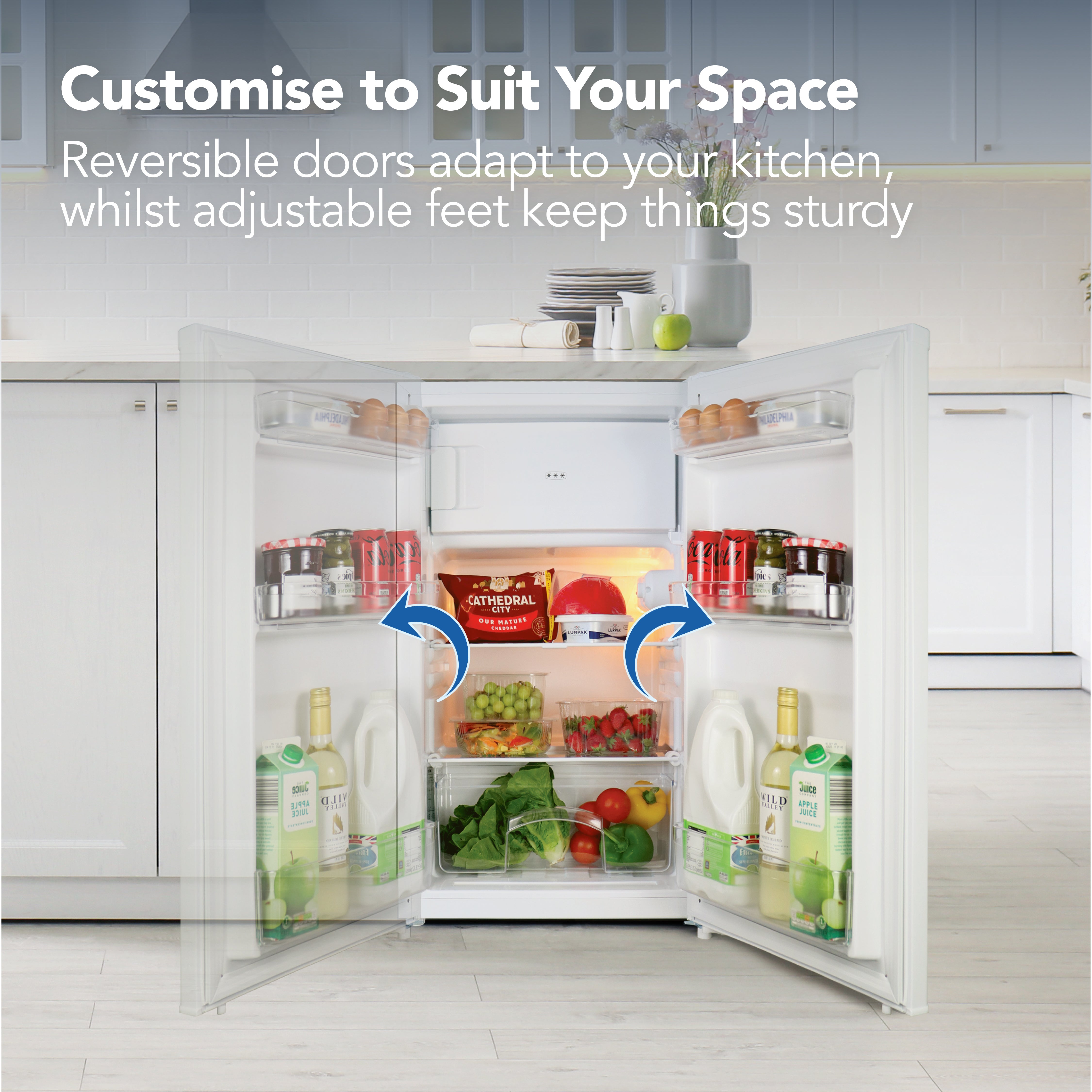 An open Igenix Under Counter Fridge with Ice Box (81 L, White) shows milk, juice, fruit, and canned drinks inside. Blue arrows highlight its reversible doors. Customizable features and the fridge’s compact design suit any kitchen décor.