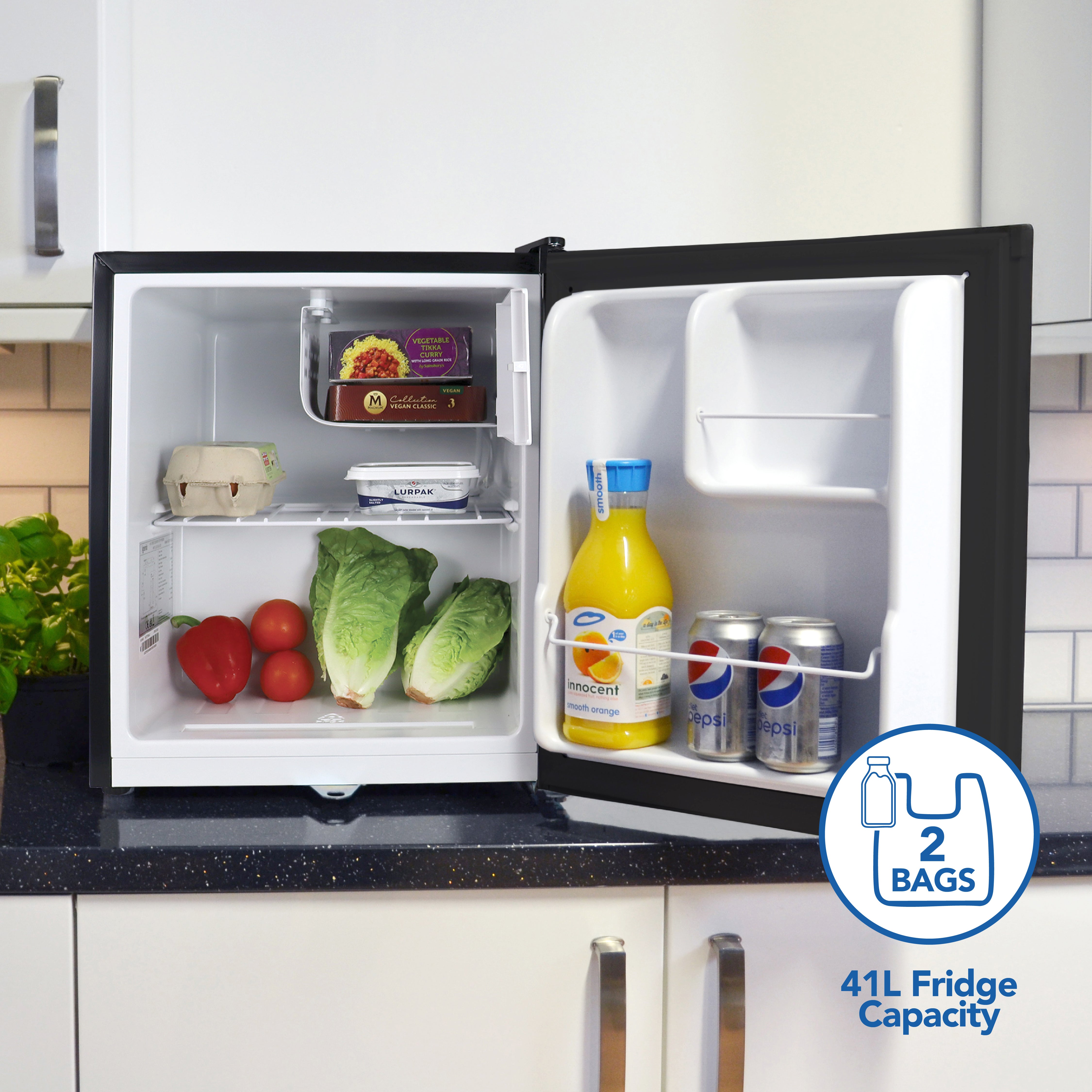 An open Igenix Table Top Fridge with Lockable Door, 41L, Black, sits on a kitchen counter with veggies, eggs, juice, yogurt, and Pepsi cans inside. “2 BAGS, 41L Fridge Capacity” with grocery bag icons is shown on the door.