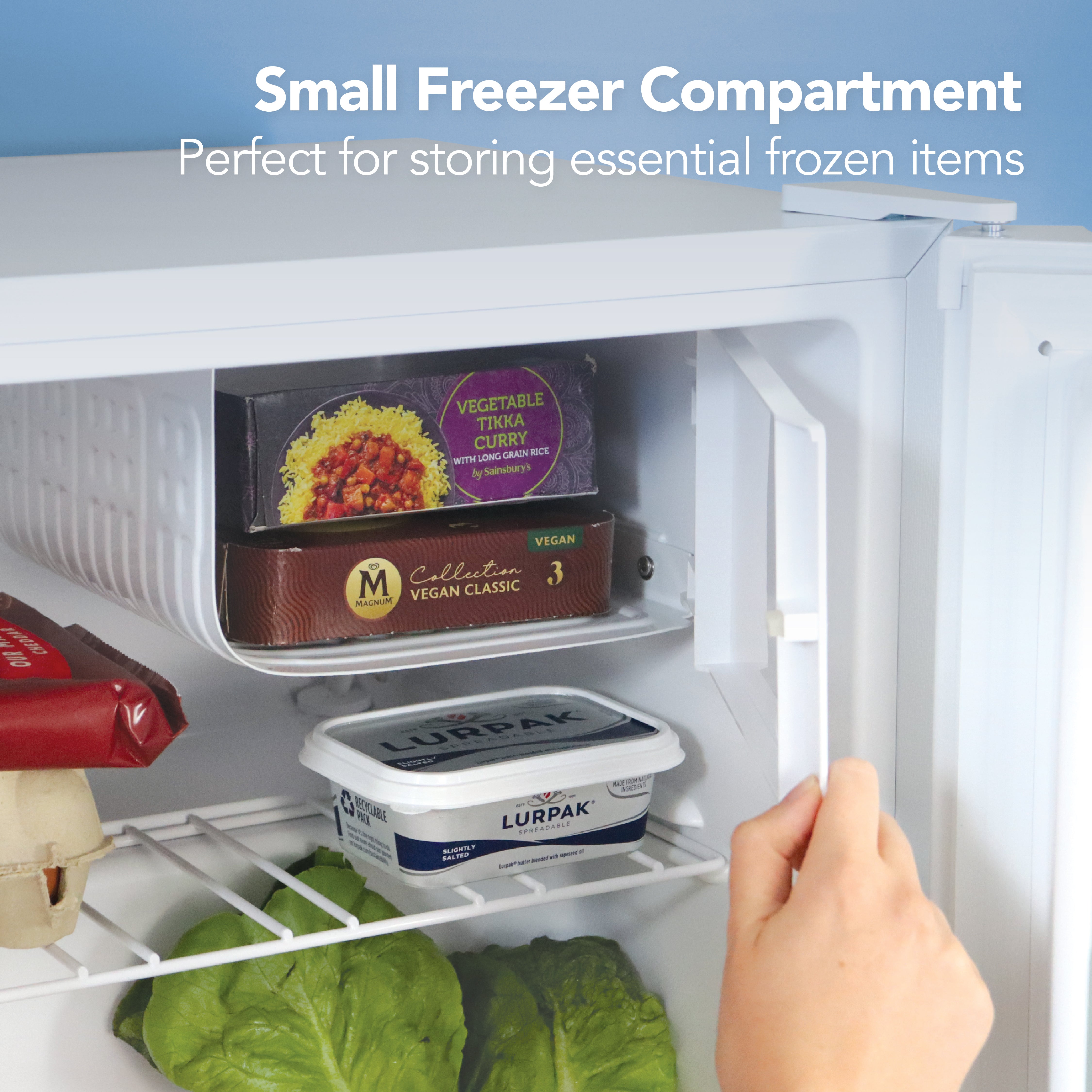 A hand opens the small freezer compartment of the Igenix 41L Table Top Fridge with Lockable Door, showing frozen food and Lurpak butter; below, lettuce and eggs are stored. Text: Small freezer – ideal for essential frozen items.