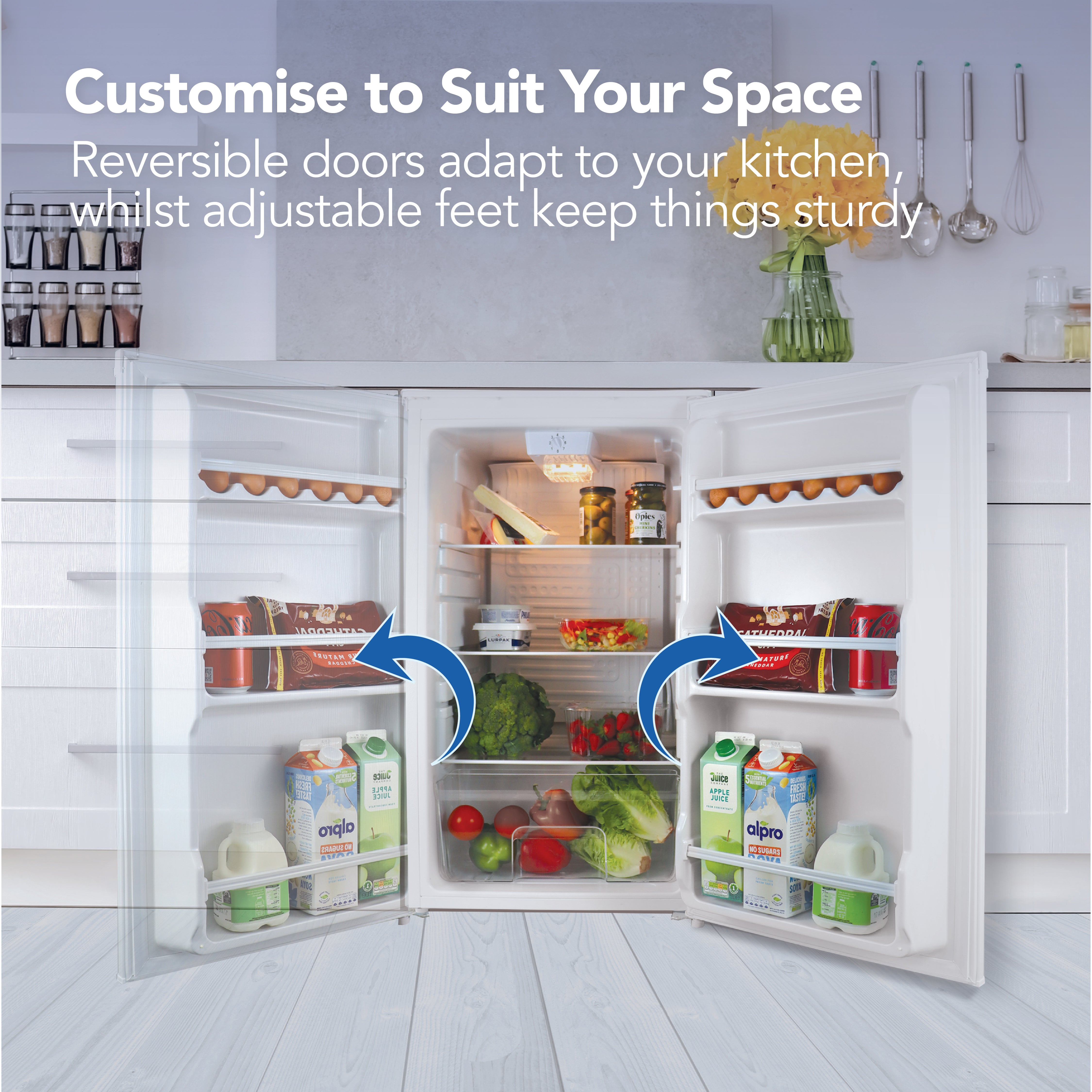 The Igenix Under Counter Larder Fridge (92L, White) is shown open in a modern kitchen with fresh food inside. Blue arrows highlight the reversible doors. Customizable features make it perfect for home offices or any small kitchen.