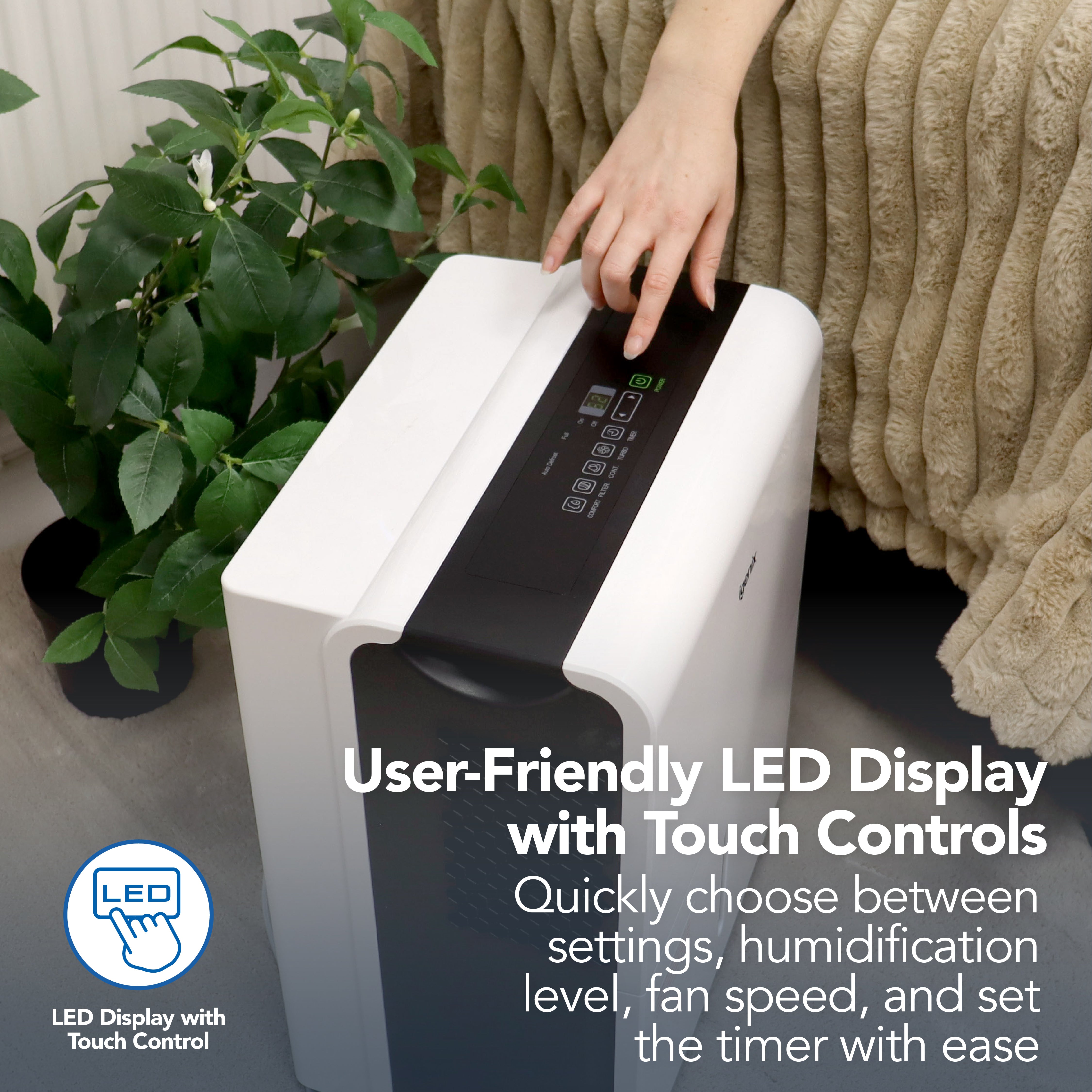 A hand adjusts touch controls on the white Igenix Portable Dehumidifier (extracts 30 litres/day) with user-friendly LED display, beside a green potted plant and beige rug. Text highlights easy settings adjustment.