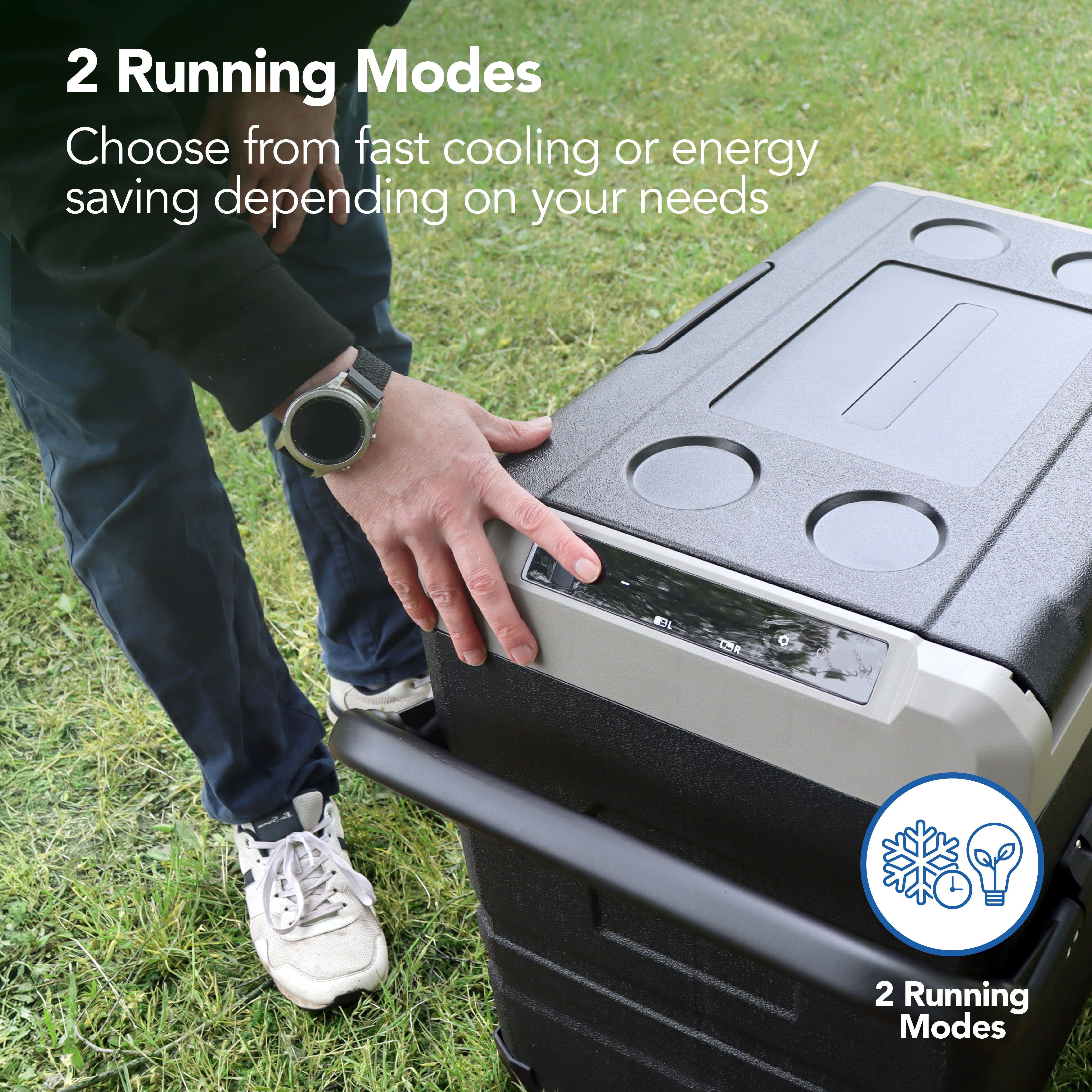 A person adjusts the Igenix 60L Portable Fridge Freezer, Black, on grass. Text: 2 Running Modes—choose fast cooling or energy saving to suit your needs. Cooling and energy mode icons are displayed.