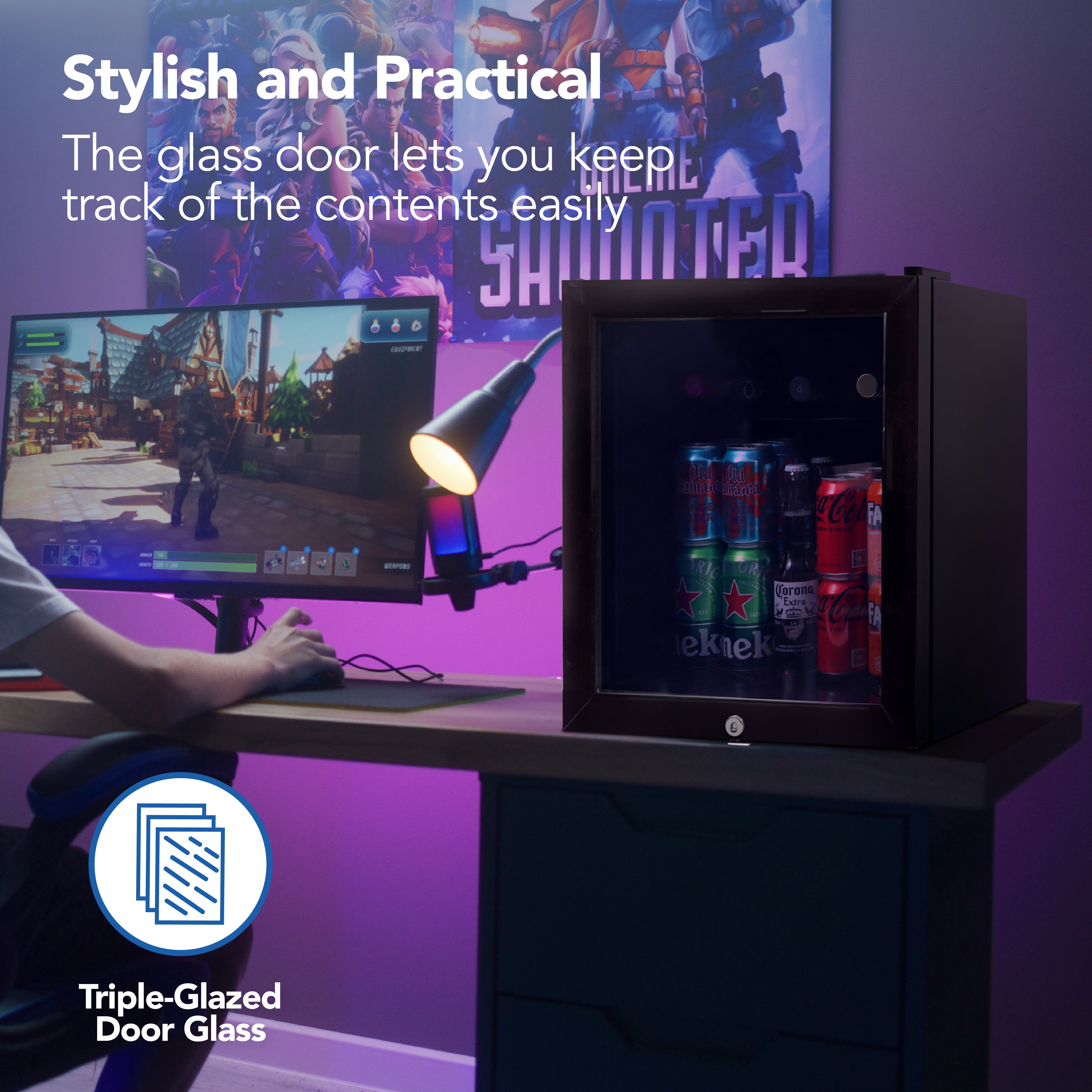 The Igenix Tabletop Drinks Fridge, 48 Litre, Black, with a triple-glazed glass door, sits on a desk beside a gamer at their computer. Colorful lighting and gaming posters decorate the background.