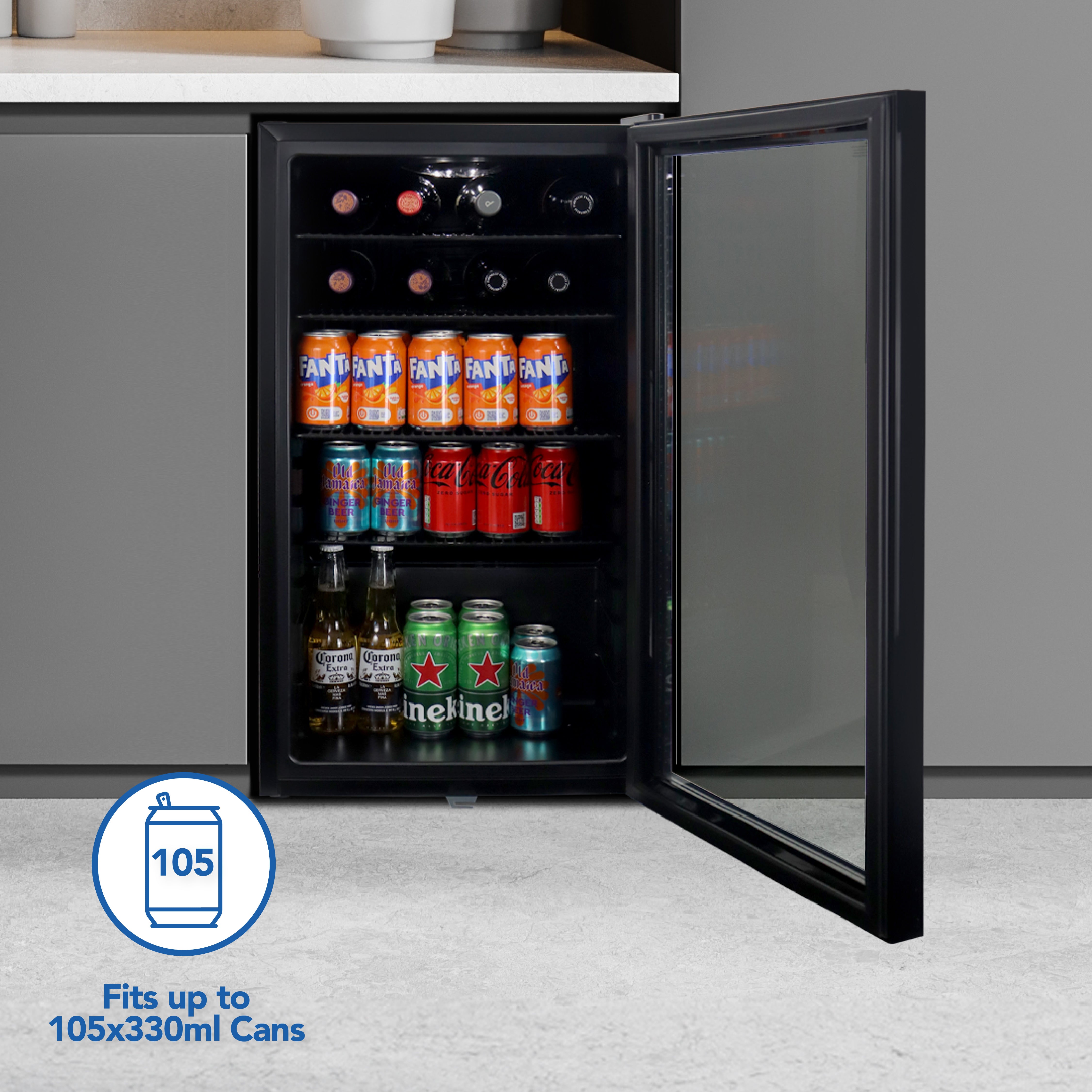 The Igenix Under Counter Drinks Fridge, 98 Litre, in black features a glass door and open shelves stocked with bottles and 330ml cans of Fanta, Coca-Cola, and Heineken. It fits up to 105 cans—ideal for keeping your drinks cold.