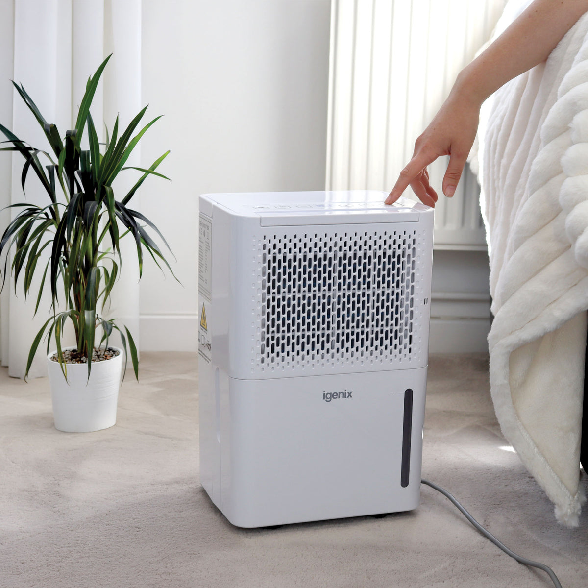 A hand touches the control panel on top of a white Igenix Portable Dehumidifier, Extracts 12 Litres per Day, White.