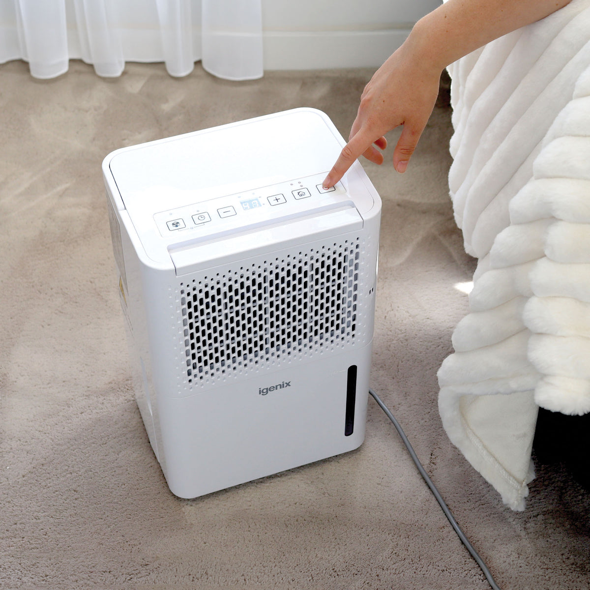 A finger pressing a button on the control panel of a white Igenix Portable Dehumidifier, Extracts 12 Litres per Day.