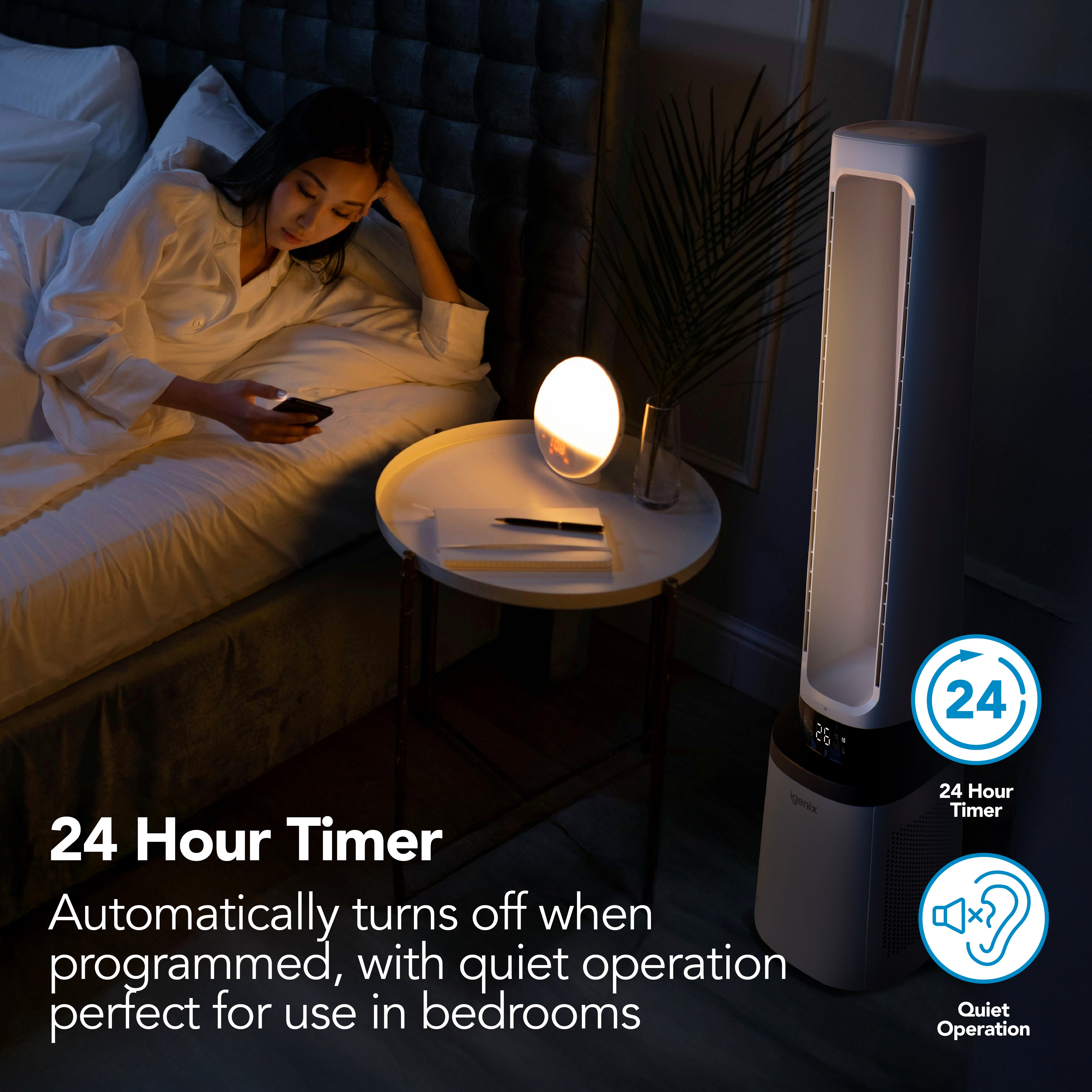 A woman in bed uses her phone next to a nightstand with a lamp and the Igenix 41 Inch Bladeless Tower Fan with Air Purifier, model IGFD02549W. Text highlights the 2-in-1 cooling tower fan’s advanced HEPA filter, quiet operation, and convenient 24-hour timer—making this innovative Igenix air purifier ideal for bedrooms.
