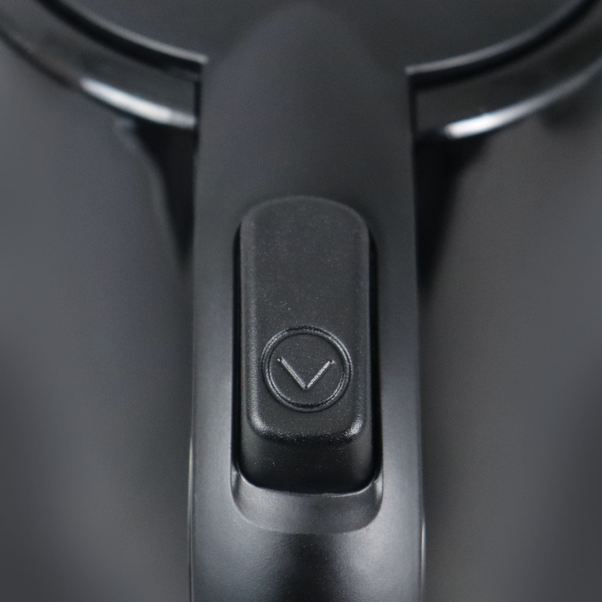 Close-up of the black plastic handle on the Igenix 1 Litre Cordless Jug Kettle (2200W), featuring a rectangular button with a downward-pointing arrow symbol—a hallmark of its energy-efficient design. Both the dark background and sleek handle enhance the modern aesthetic of this Igenix appliance.