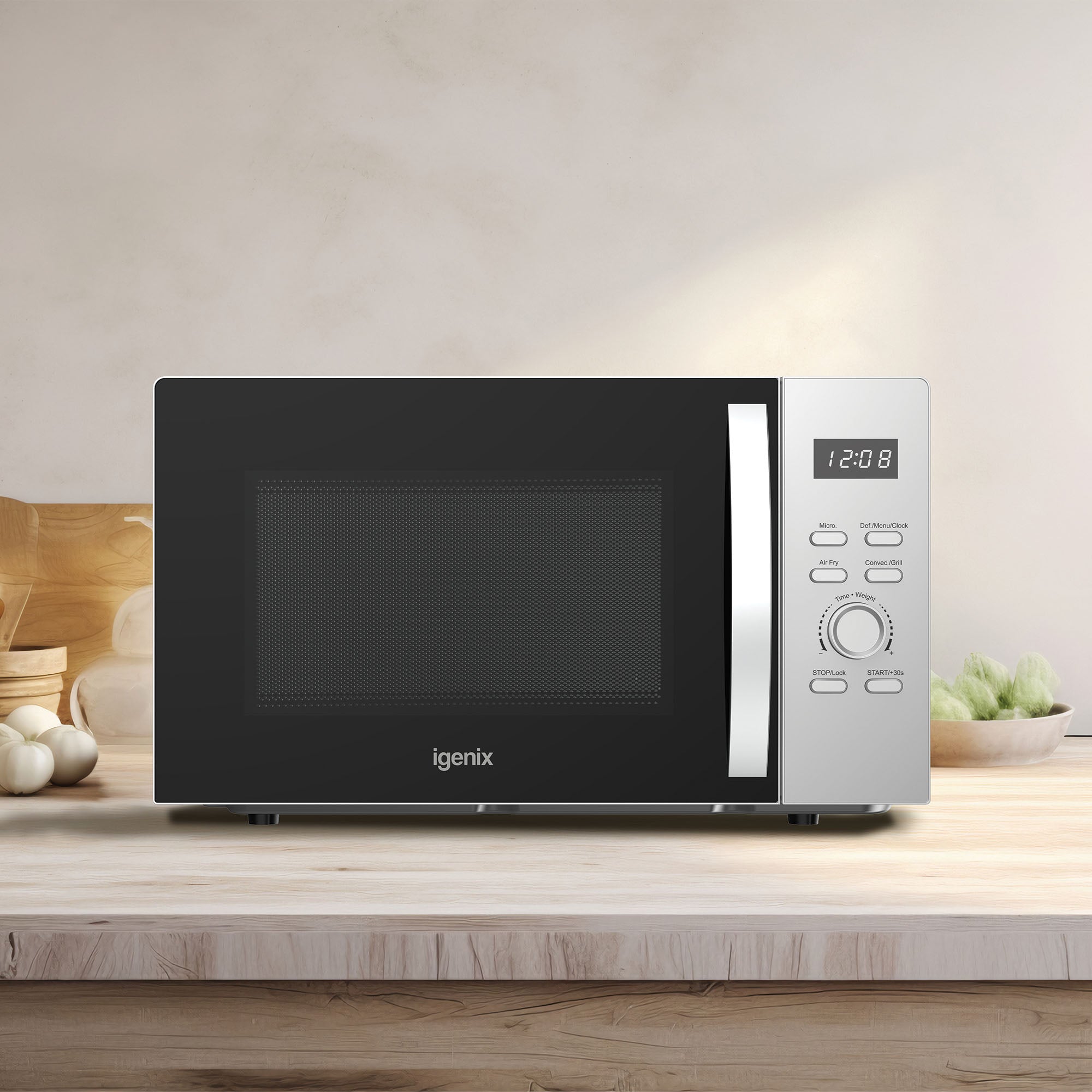 An Igenix Microwave with Air Fryer Function (28L, 900W, Silver, IGMC02890S) sits on a wooden kitchen counter at 12:08, surrounded by vegetables and kitchen items that showcase its versatile design.