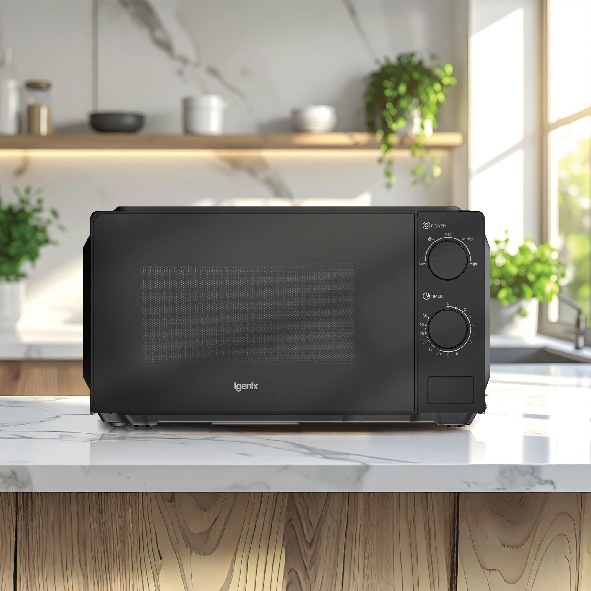 An Igenix IGMS02071B black manual microwave (700W, 20L, 35-min timer) sits on a marble kitchen countertop with green potted plants, wooden shelves, and a large sunlit window in the background.