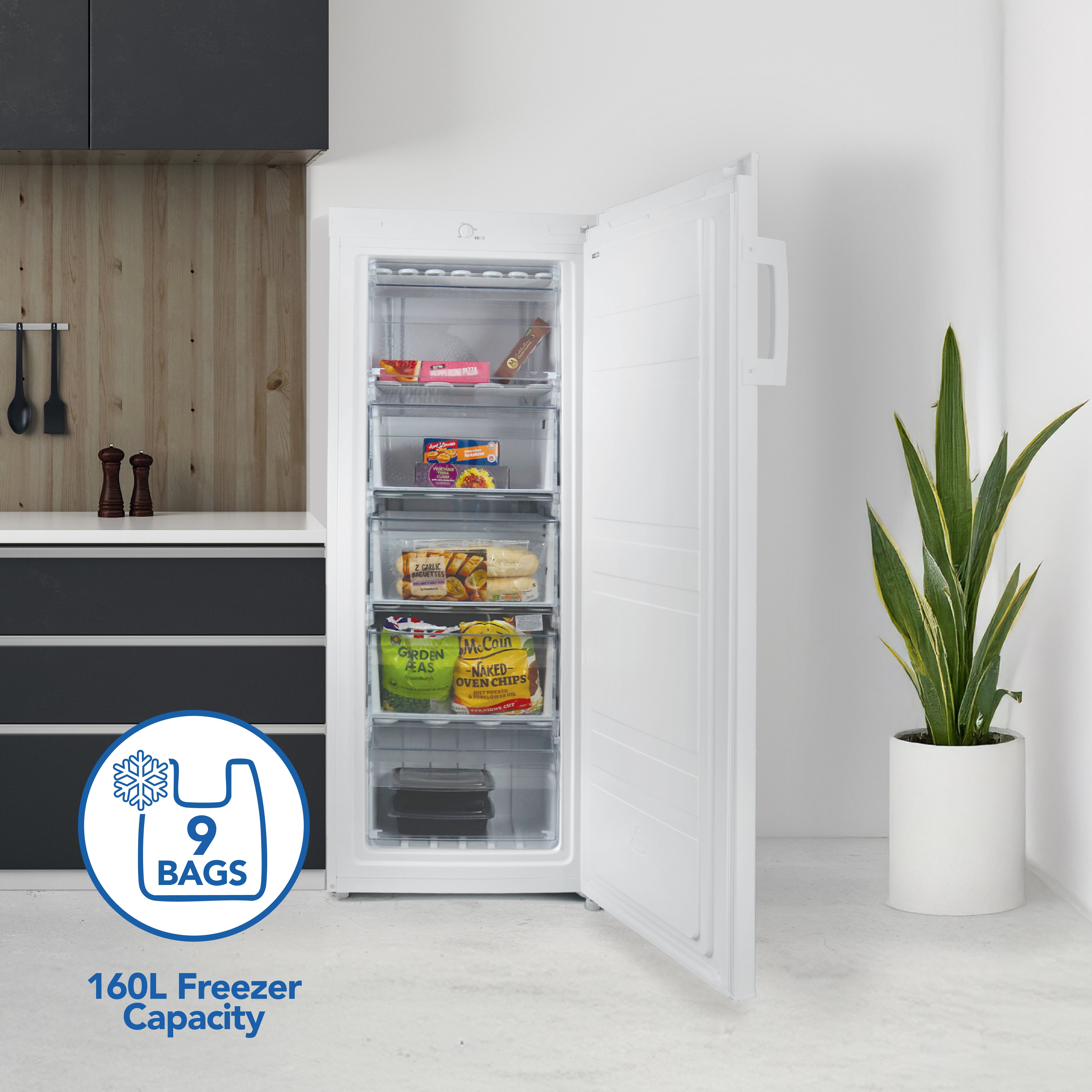 An open Igenix Freestanding Tall Freezer, 55cm wide with a 160L capacity, displays four food-filled shelves in a modern kitchen. A plant sits nearby. Text overlay reads: "9 bags, 160L freezer capacity.