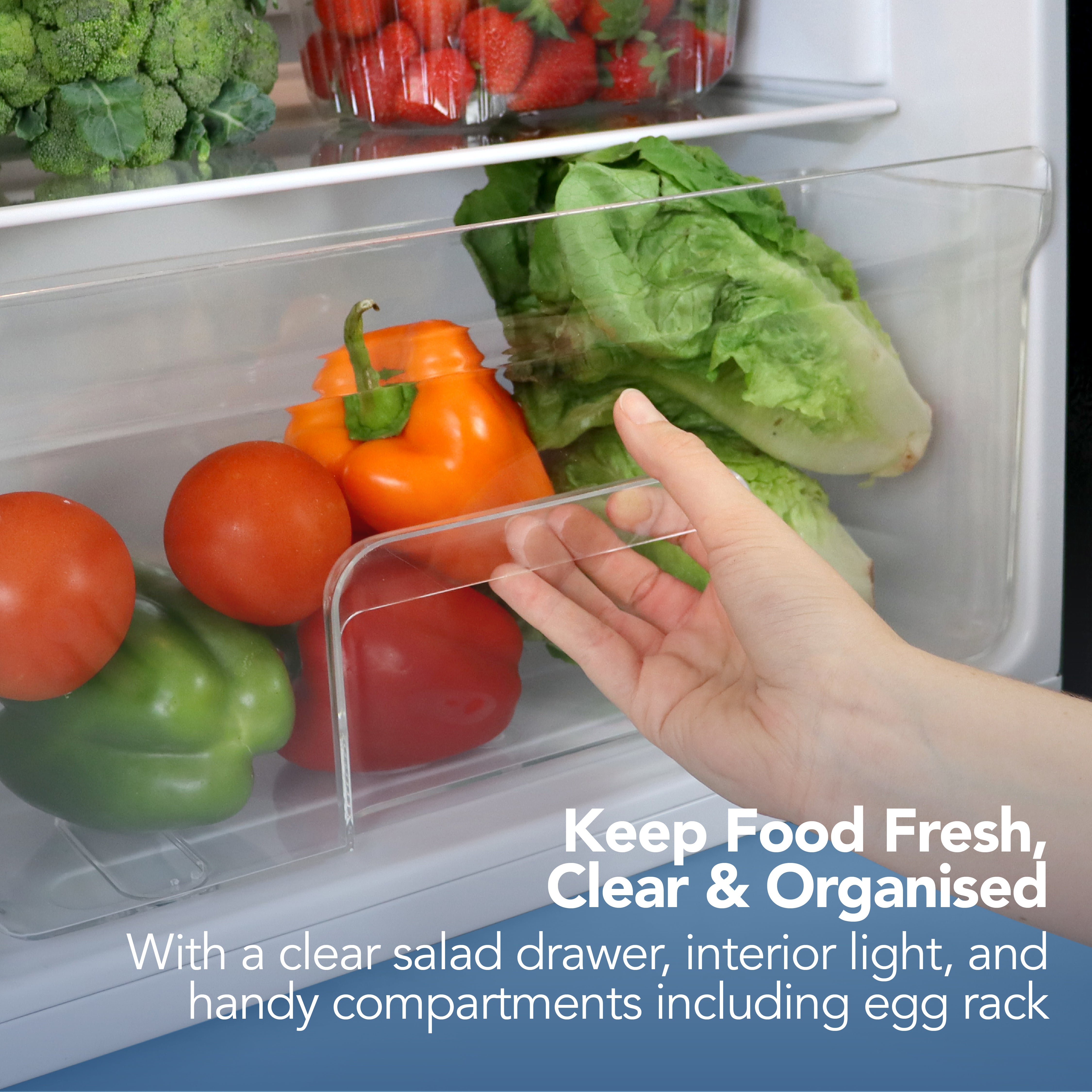 A hand opens a clear salad drawer in the Igenix Under Counter Larder Fridge (92L, Black), showing bell peppers, tomatoes, and lettuce. Text: Keep food fresh, clear & organised with features like reversible door, interior light, and egg rack.