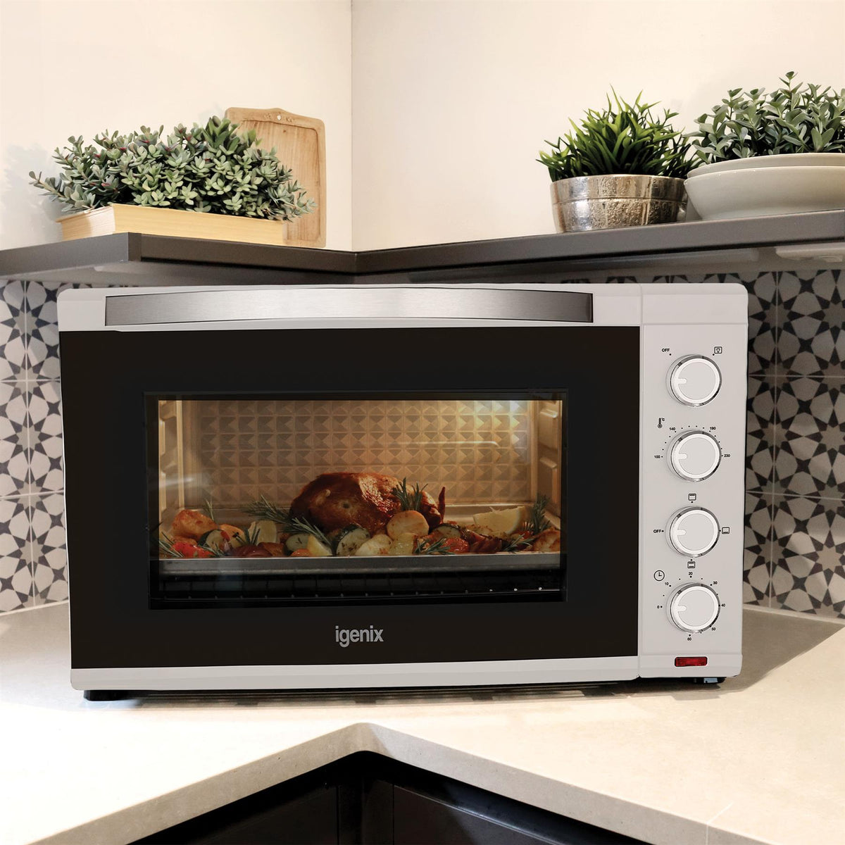 White 60L Mini Oven by Igenix on a kitchen counter with a roast chicken and vegetables cooking inside.