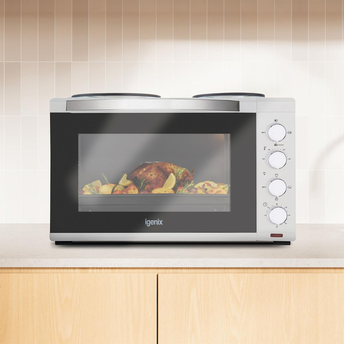 White Igenix 48L Mini Oven with Hotplates, featuring a glass door showing a roasted chicken and potatoes inside, and a control panel with four dials on the right.