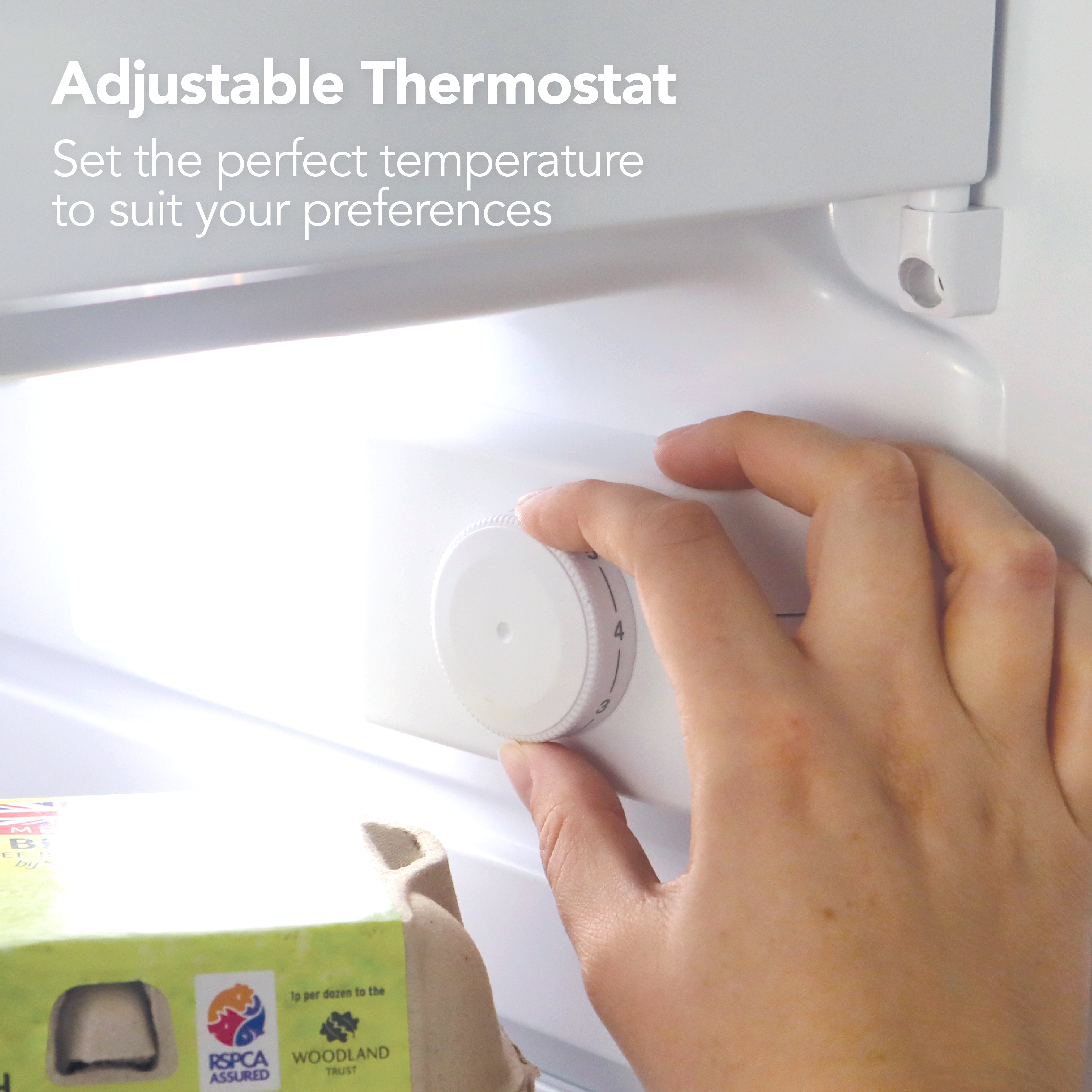 A hand turns the adjustable thermostat inside the Igenix Under Counter Fridge with Ice Box, Inox. Text above reads: "Adjustable Thermostat – Set your perfect temperature." An egg carton is visible in the foreground.
