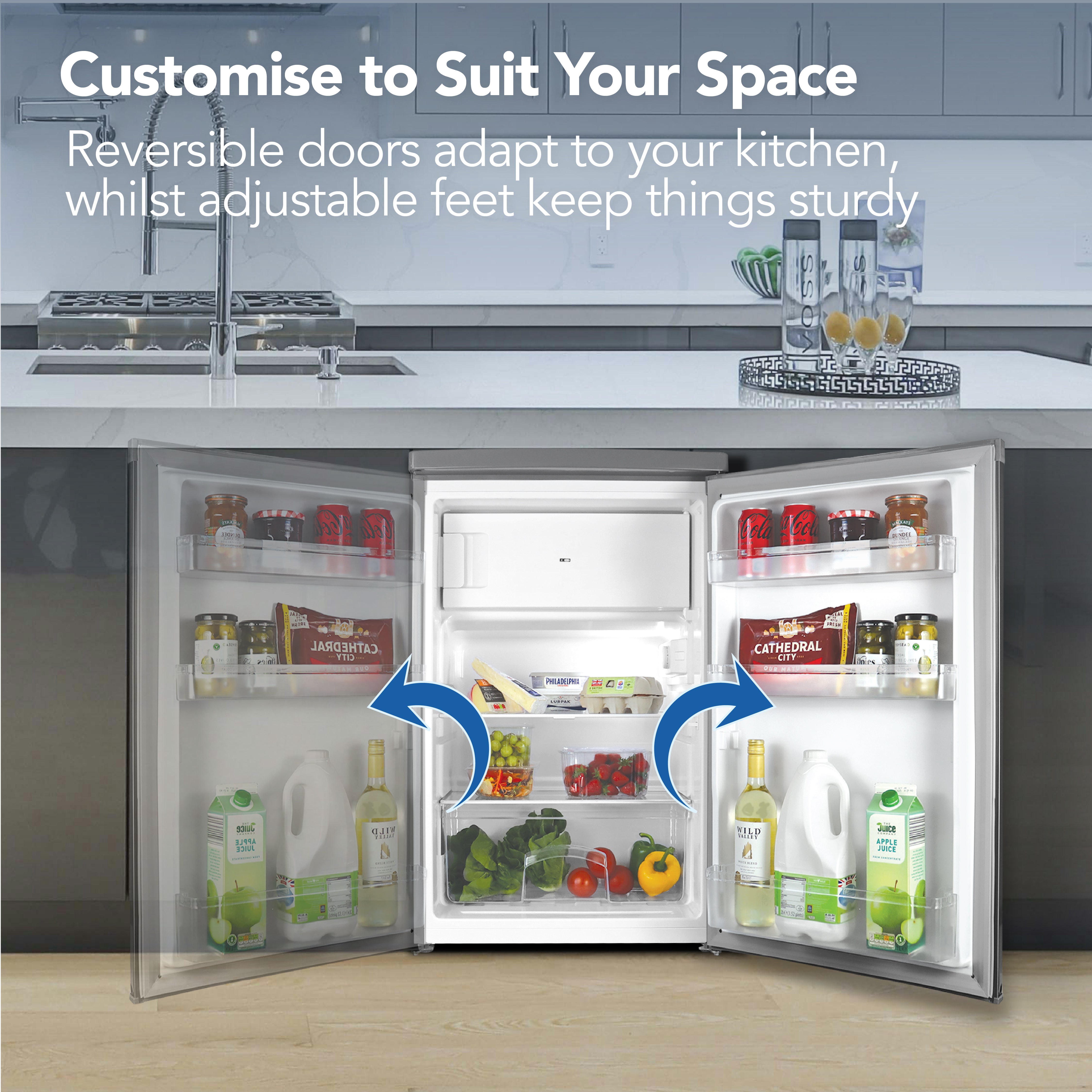 The Igenix Under Counter Fridge with Ice Box (Inox) sits open in a modern kitchen, filled with groceries and drinks. Blue arrows show its reversible doors. Customizable doors, adjustable feet, and a handy 4* ice box are highlighted above.
