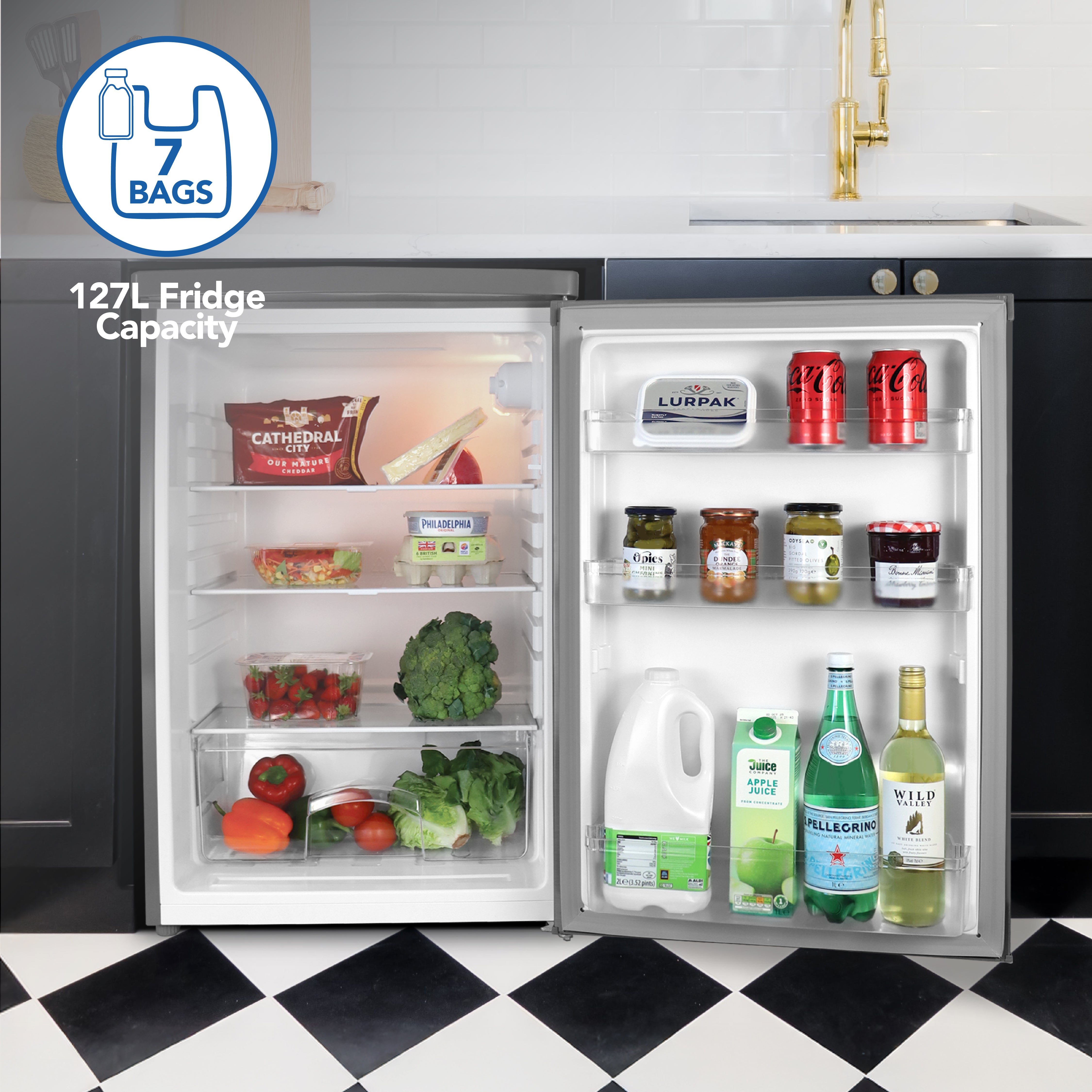 The Igenix Under Counter Larder Fridge, 127 Litre in Silver, stands open on a sleek kitchen floor, stocked with groceries. Its reversible door displays bottles and cans, while a "7 bags" graphic shows off its impressive capacity.
