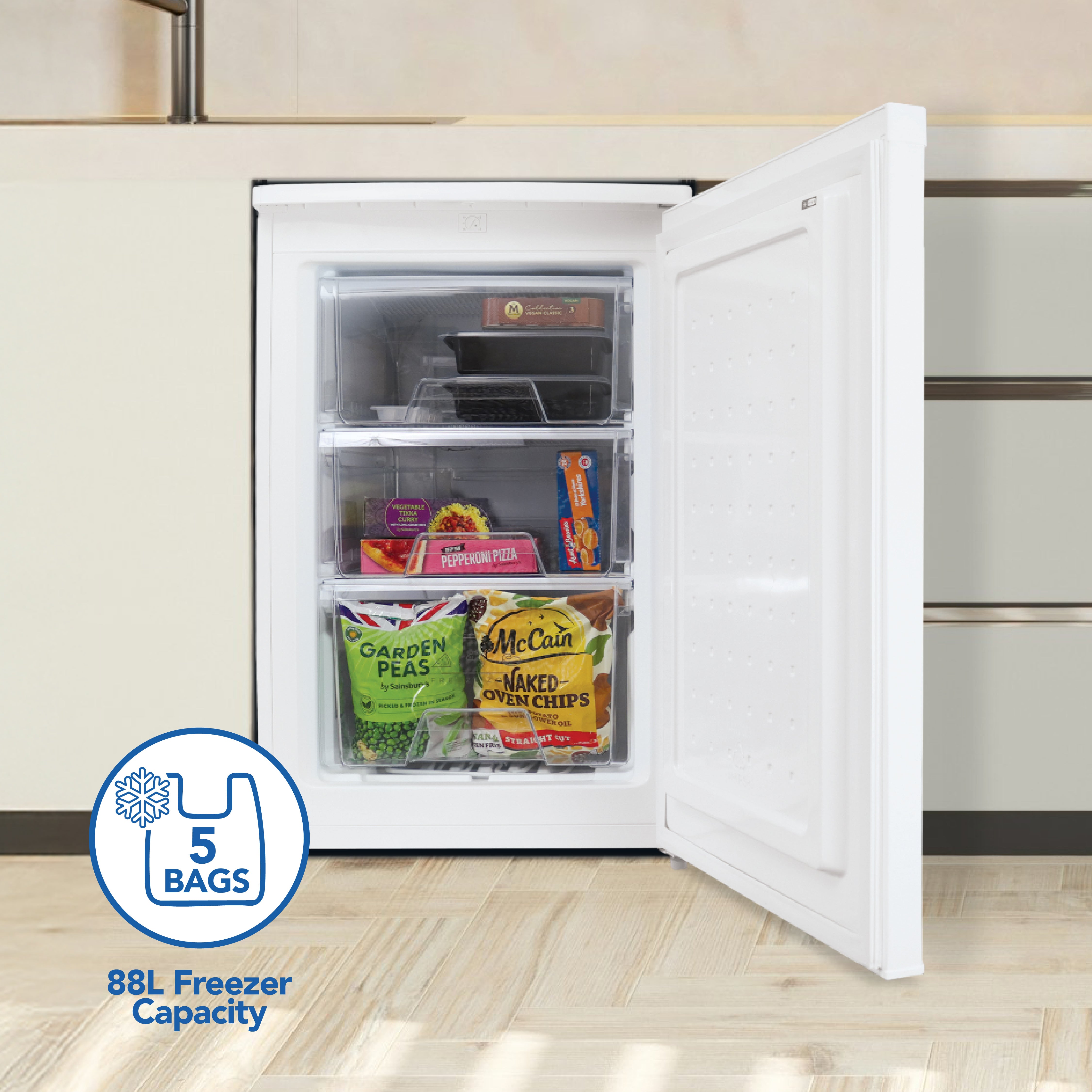An Igenix Under Counter Freezer (88L, reversible doors, white) is open in a kitchen, showing three spacious drawers stocked with frozen food. A graphic highlights its 5-bag storage and 88-litre capacity.