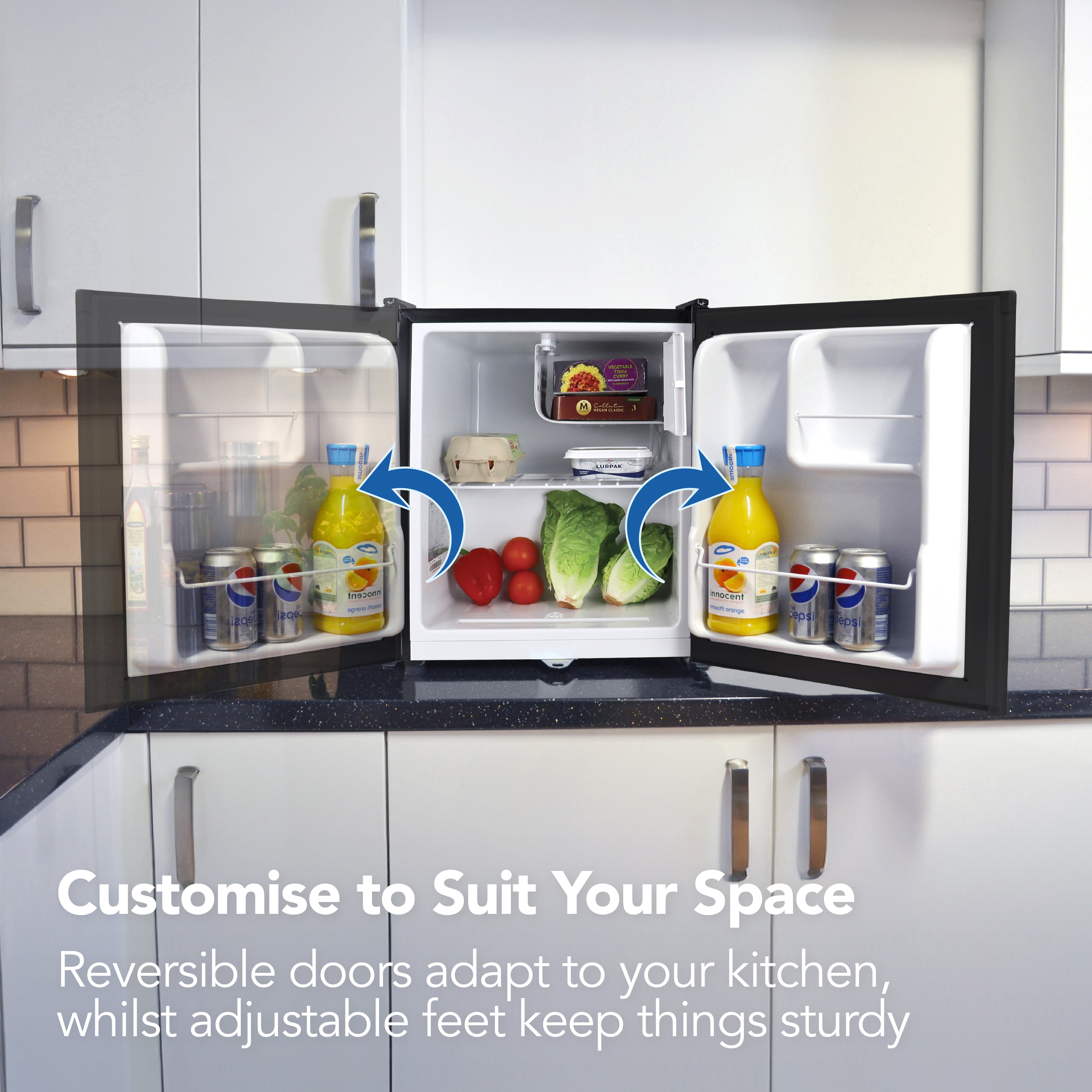 An open Igenix Table Top Fridge with Lockable Door, 41 Litre, Black sits in a kitchen, stocked with juice bottles, lettuce, tomatoes, and cans. Reversible doors and adjustable feet make it ideal for small kitchens and custom layouts.