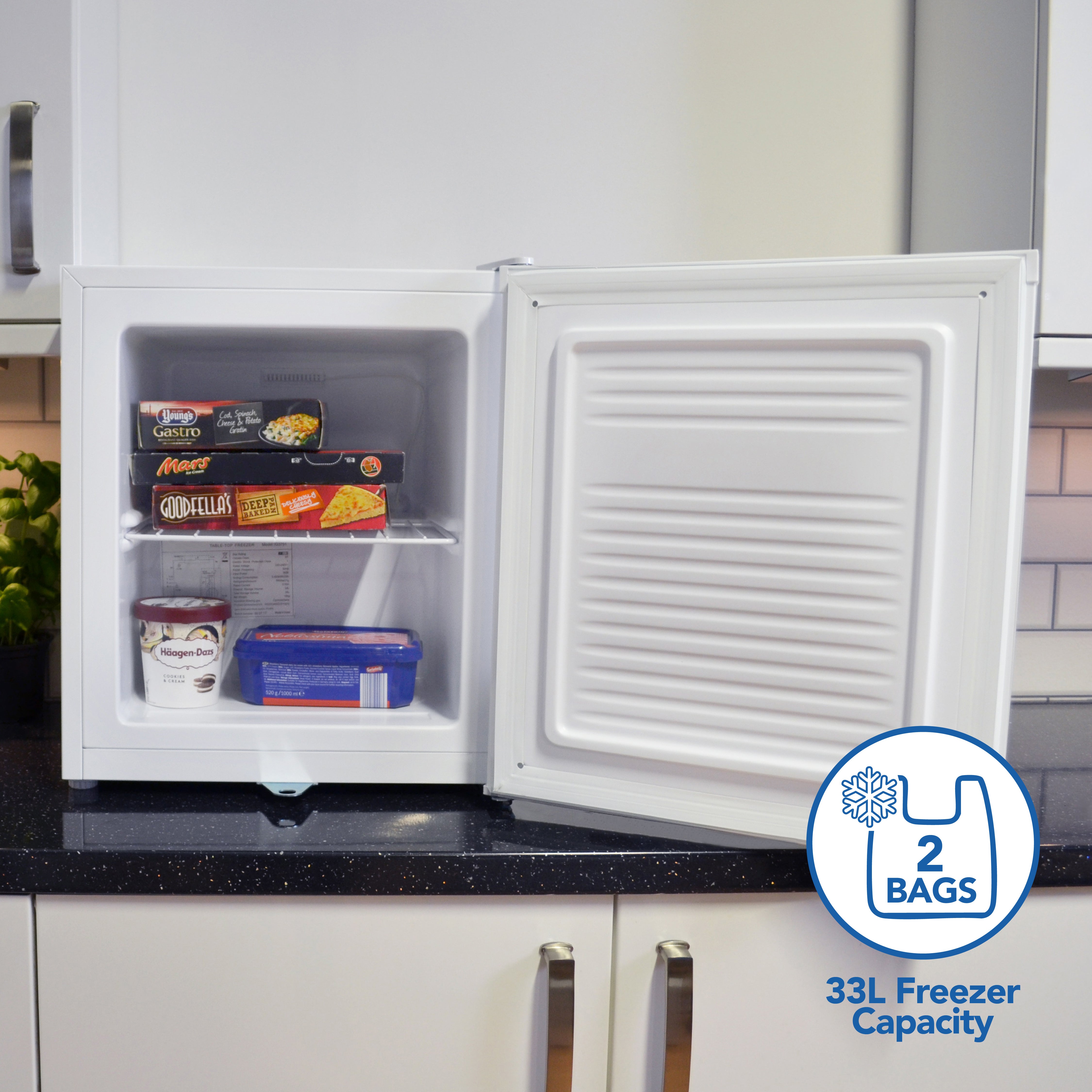 A compact Igenix Table Top Freezer with a lockable door and 33 litre capacity sits on the counter, stocked with frozen foods and ice cream. A sticker highlights its space-saving design and generous freezer space.