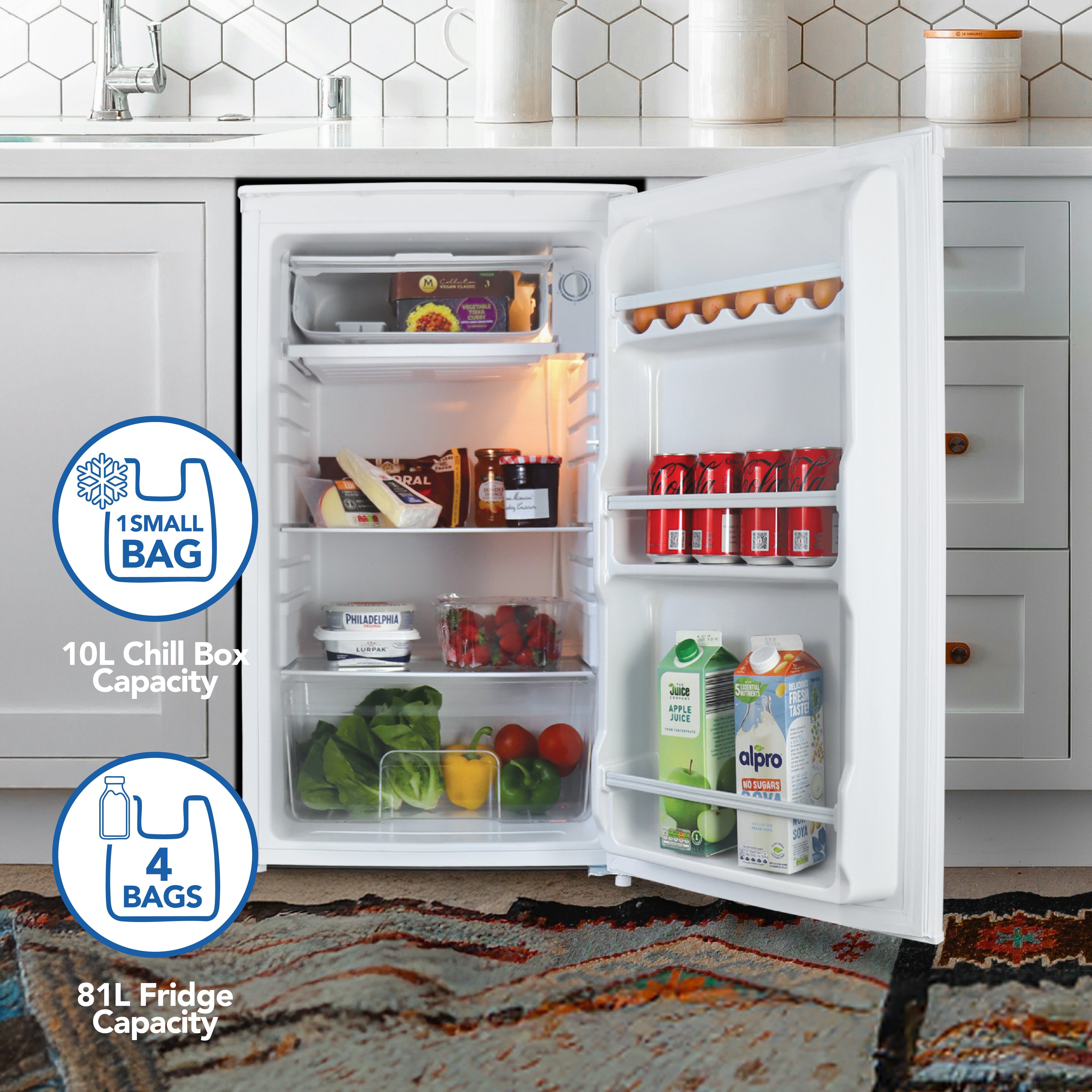 An open white Igenix Under Counter Fridge with Chill Box, 91L, stands in a modern kitchen filled with veggies, eggs, cans, juice cartons, and packaged foods. Infographics show a 10L chill box and space for four shopping bags.