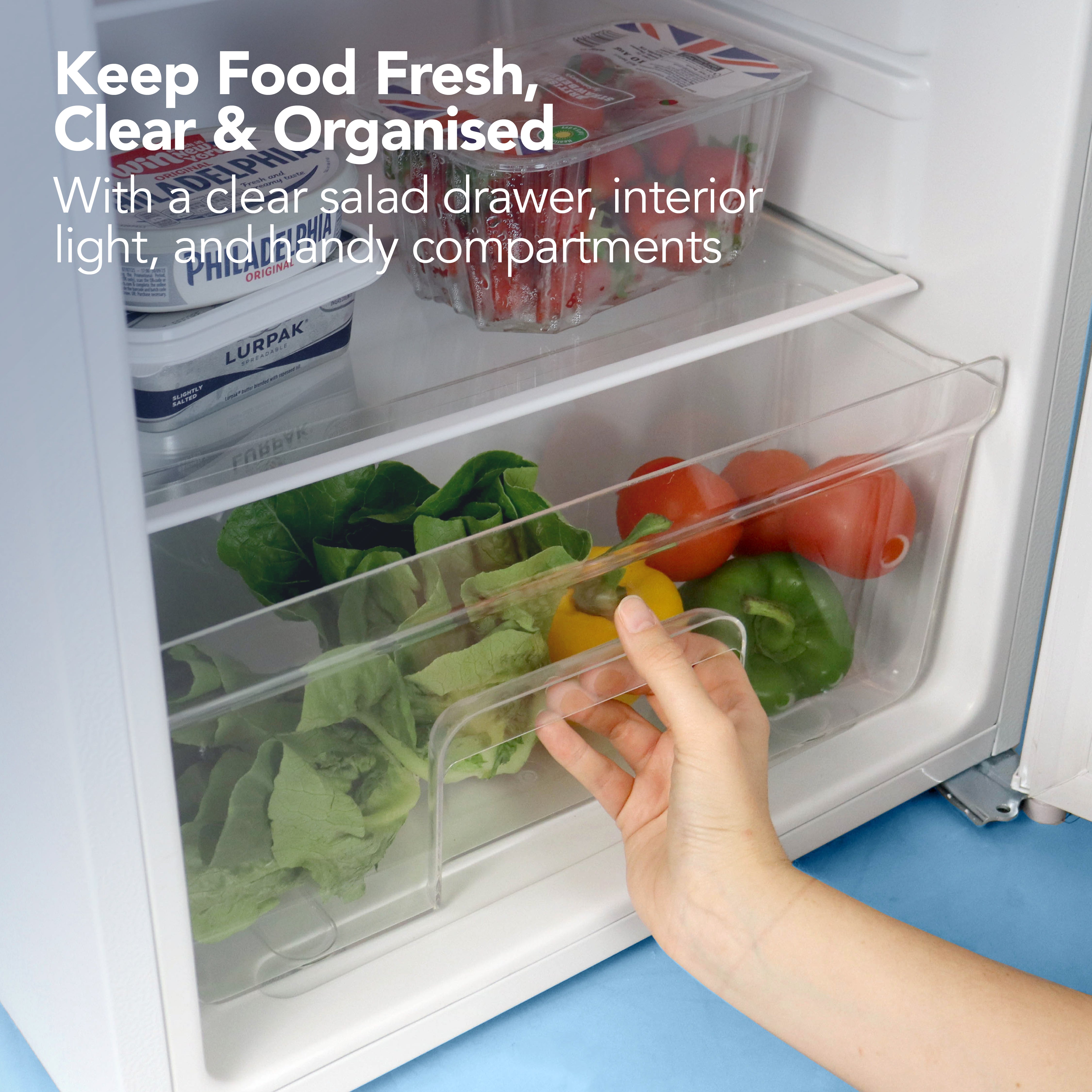 A hand opens a clear salad drawer in the Igenix Under Counter Fridge with Chill Box, 91 Litre, White. Inside are lettuce, tomatoes, and a yellow bell pepper; butter and strawberries above. Text reads: Keep Food Fresh, Clear & Organised.
