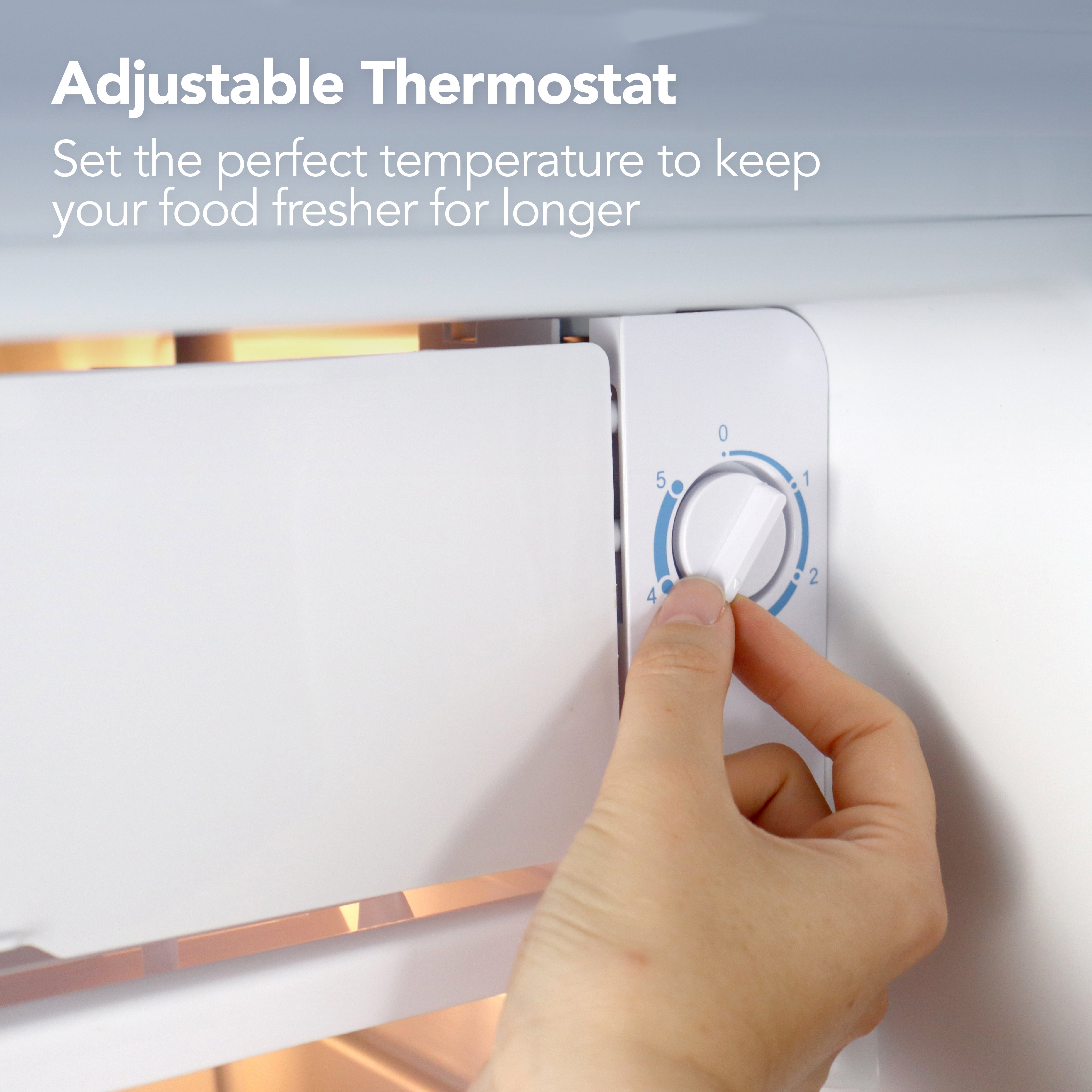 A hand turns the adjustable thermostat dial inside the Igenix Under Counter Fridge with Chill Box, 91 Litre, White. Text above reads: Adjustable Thermostat. Set the ideal temperature to keep your food fresher for longer.