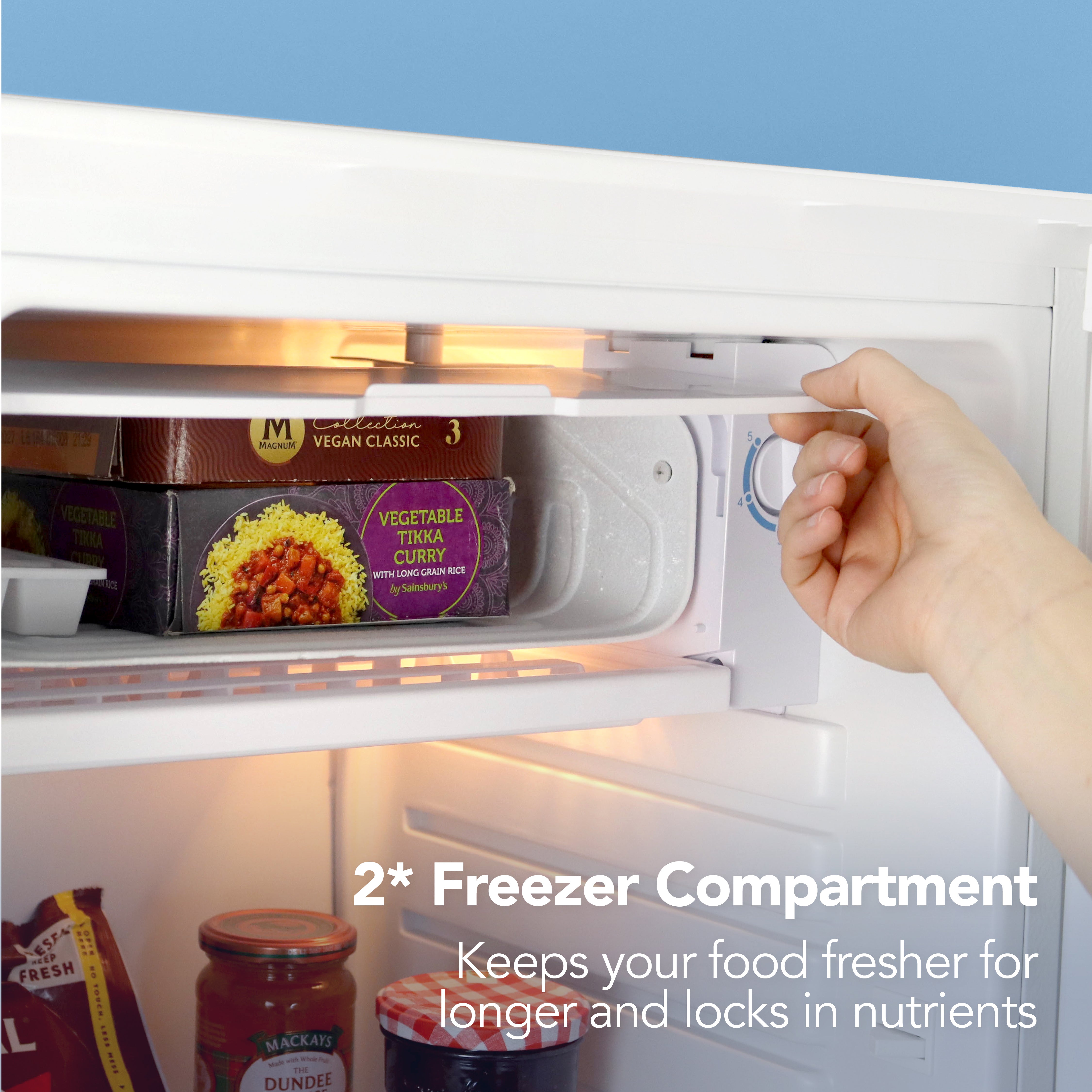A hand adjusts the temperature dial inside the Igenix Under Counter Fridge with Chill Box, 91 Litre, White, helping keep your food fresher for longer and locking in nutrients.