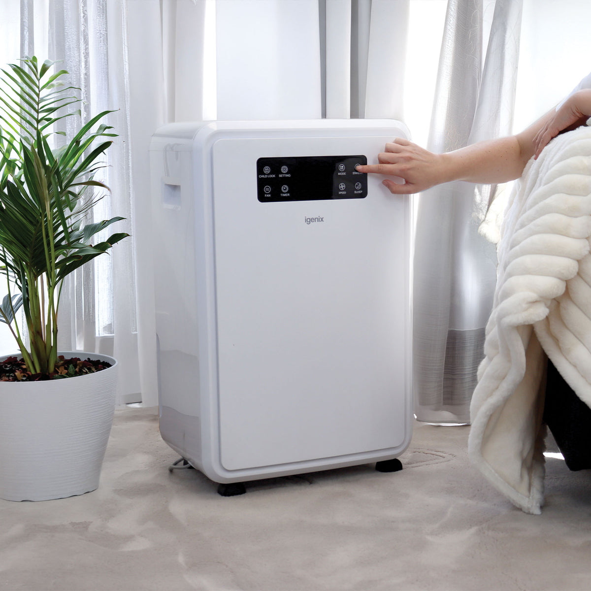 A person presses the control panel button on a white Igenix Portable Dehumidifier, Extracts 50 Litres per Day.