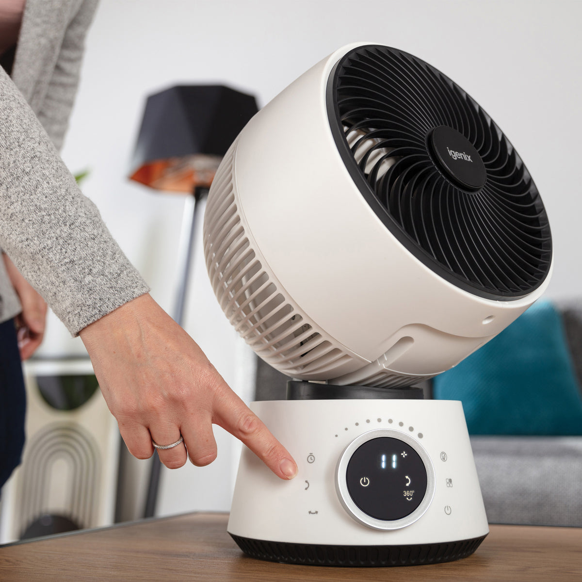 A hand presses a button on the base of a white Igenix Digital Air Circulator Turbo Fan, 9 Inch, which features a circular display showing one of its 32 wind speeds.