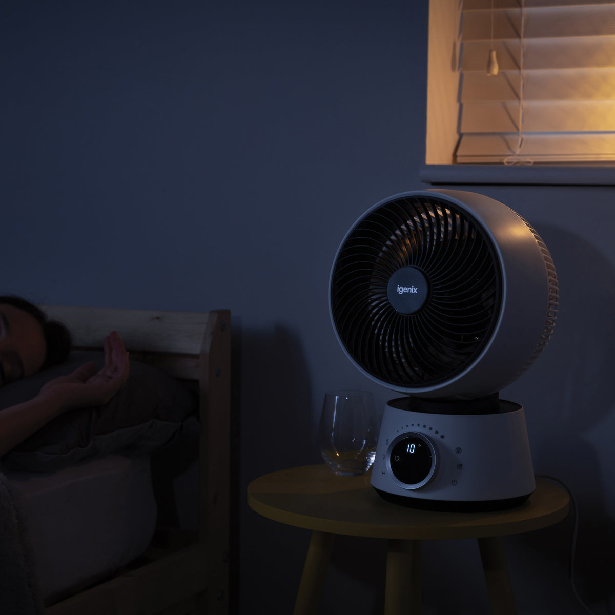 An Igenix Digital Air Circulator Turbo Fan, 9 Inch, White with a digital display and a scented oil diffusing pad sits on a bedside table next to someone sleeping.