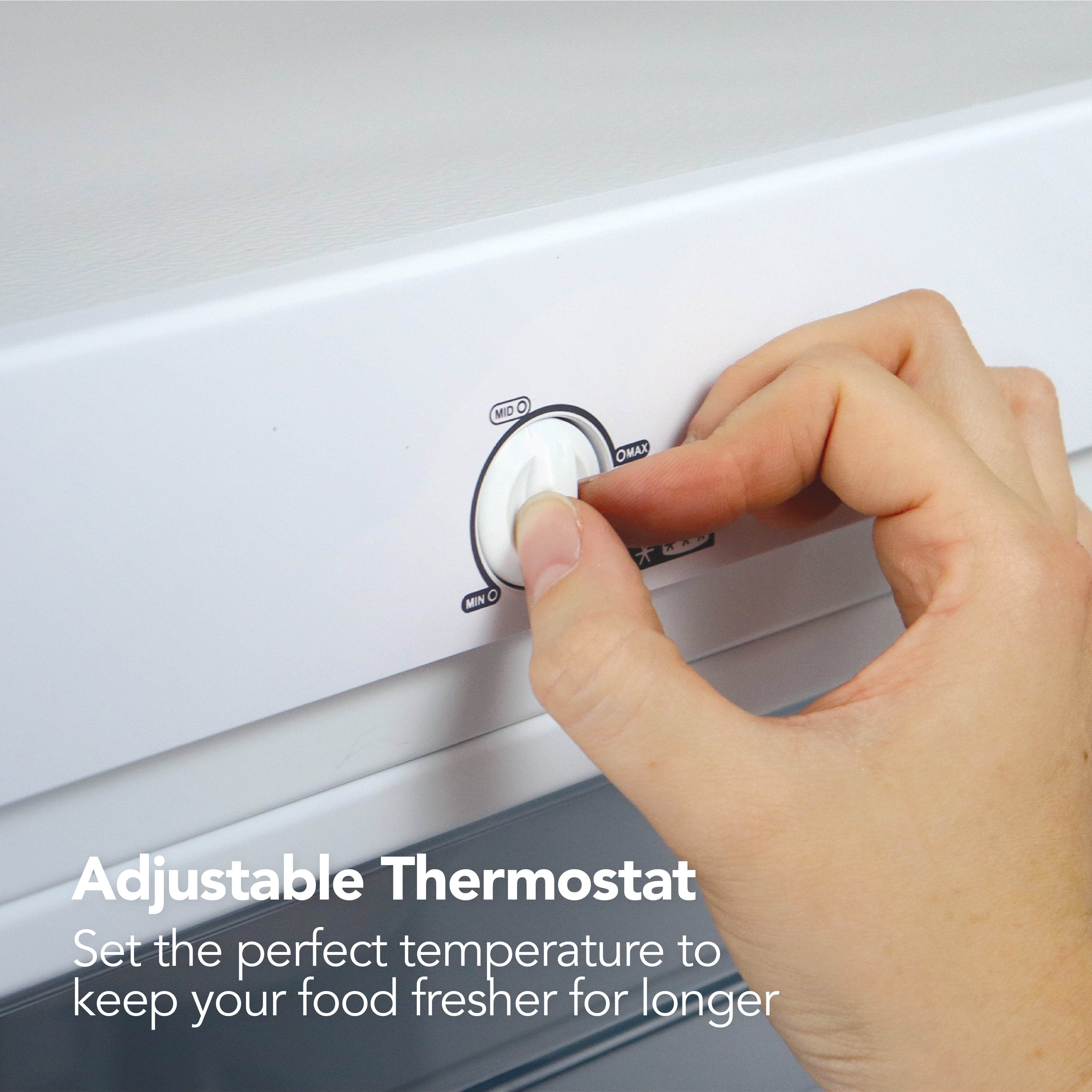 A hand turns the adjustable thermostat on the Igenix Freestanding Tall Freezer (55cm, 160L), with text: Adjustable Thermostat. Set the perfect temperature to keep your food fresher for longer.